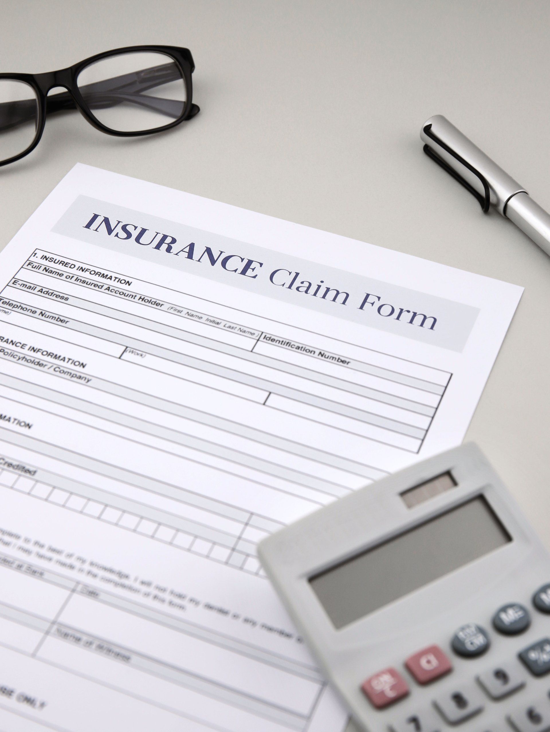 Insurance claim form on a desk with glasses, a pen, and a calculator.