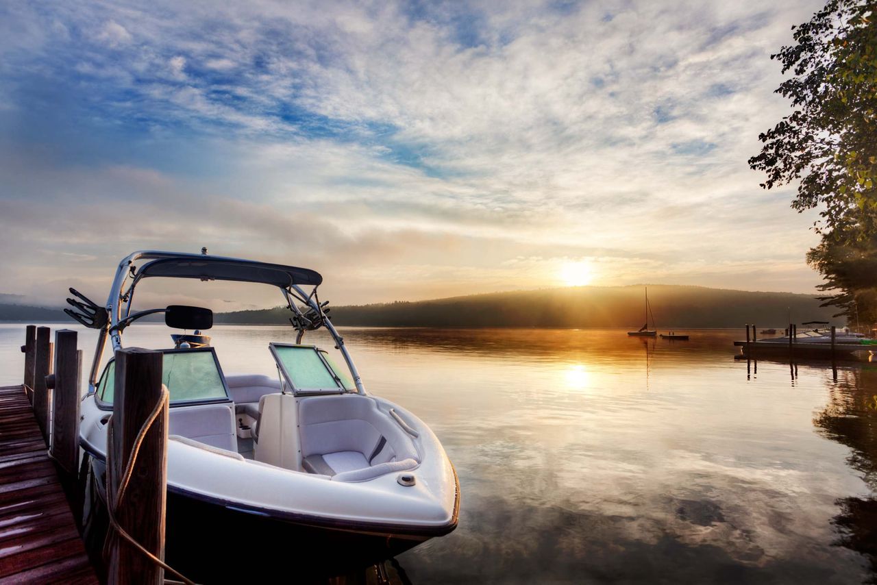 Boat docked on a lake at sunrise; calm water reflects the golden sky.