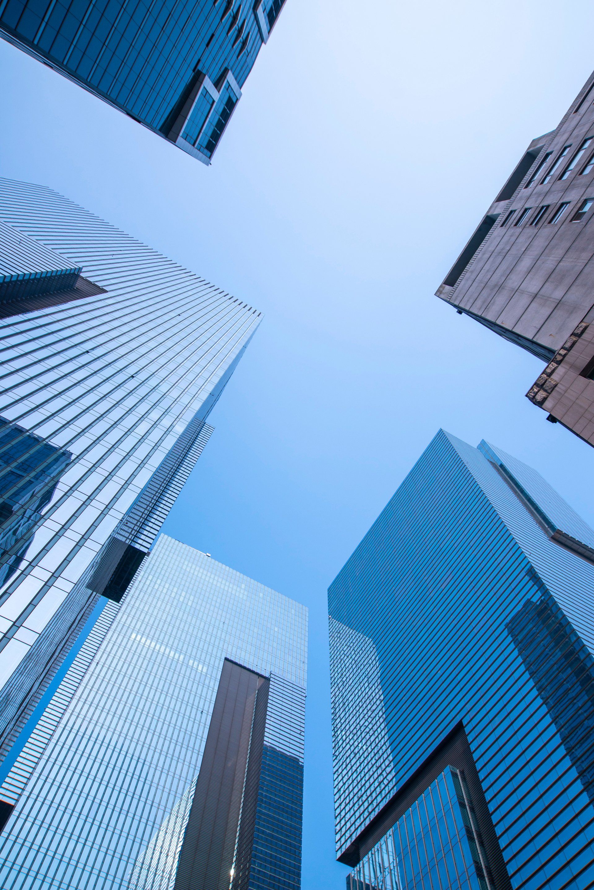 Skyscrapers with reflective glass facades against a clear blue sky, viewed from a low angle.