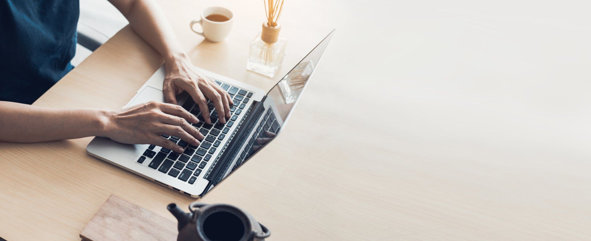 Person typing on a laptop at a desk with a coffee cup and other items.