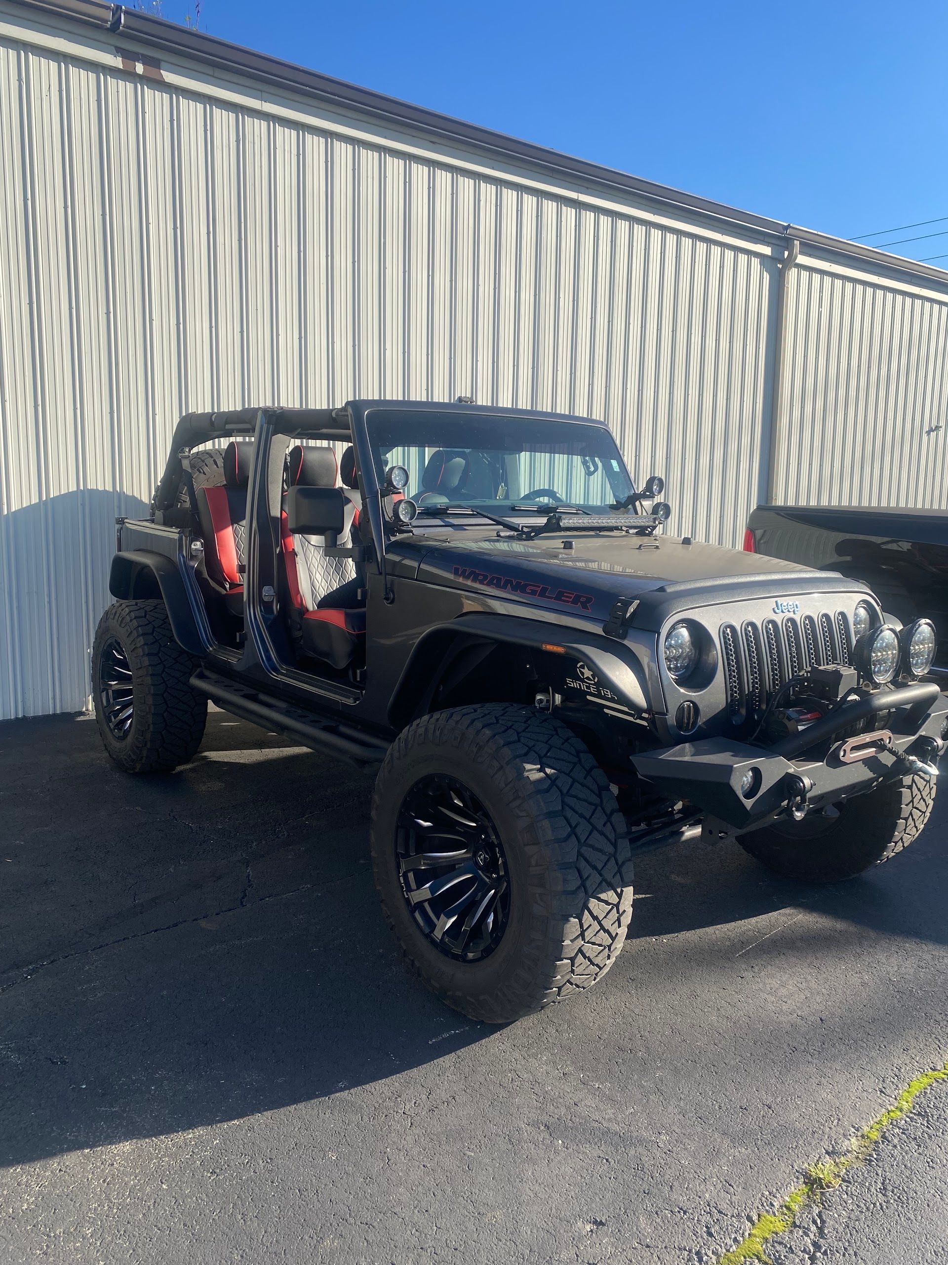 Black lifted Jeep Wrangler with doors off parked beside a corrugated metal building | Lanning Automotive & Tire