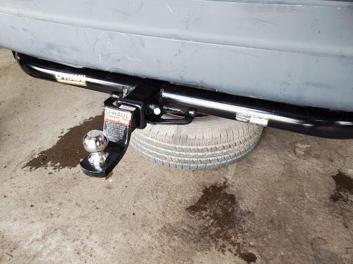 Tow hitch with a tow ball mounted under the rear of a gray vehicle, with a spare tire behind it | Lanning Automotive & Tire