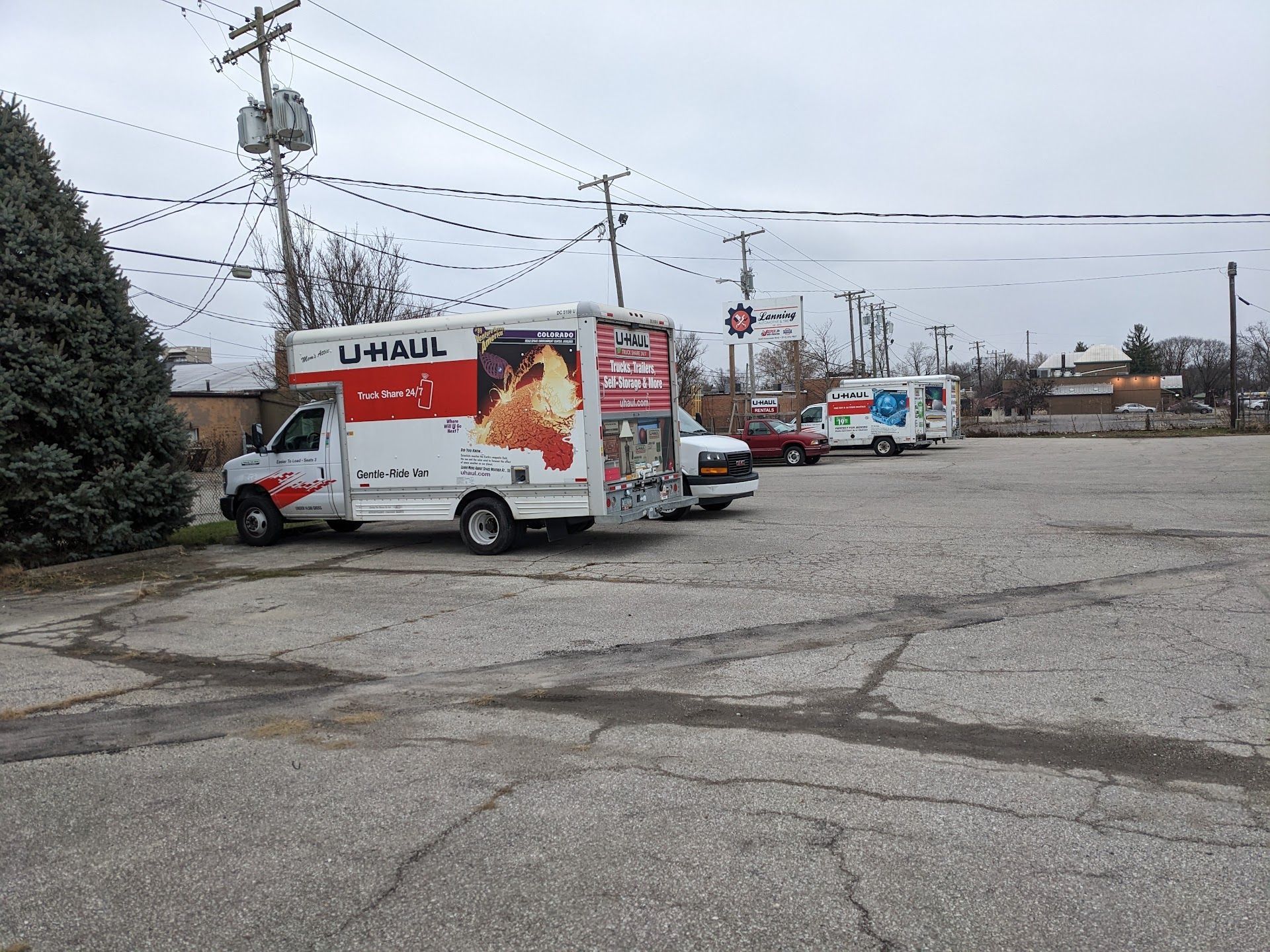 U-Haul truck and trailer parked in a cracked lot with utility poles and other vehicles under an overcast sky | Lanning Automotive & Tire