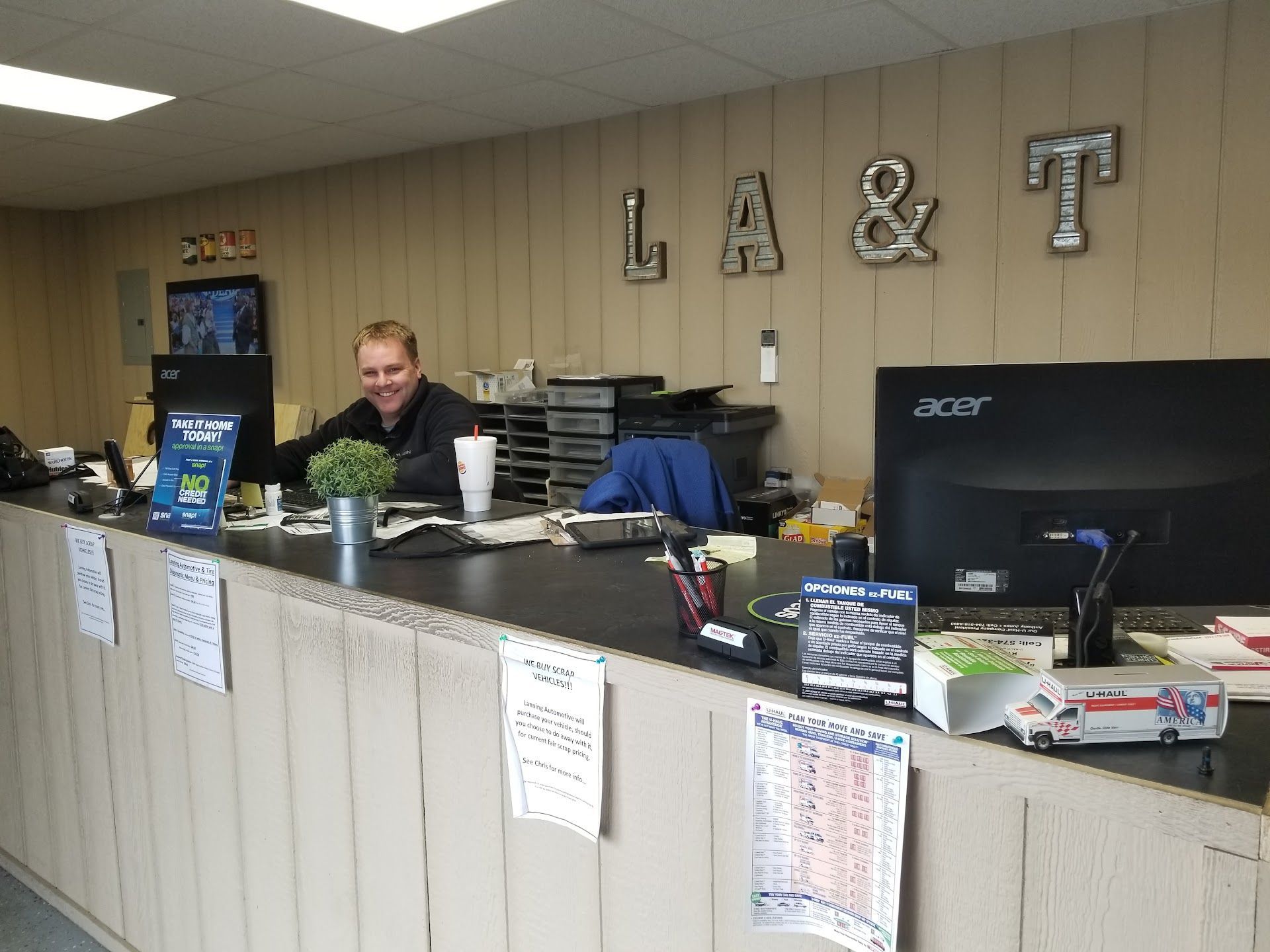 Office reception desk with a man behind the counter, computers, and large “L&T” letters on the wall | Lanning Automotive & Tire