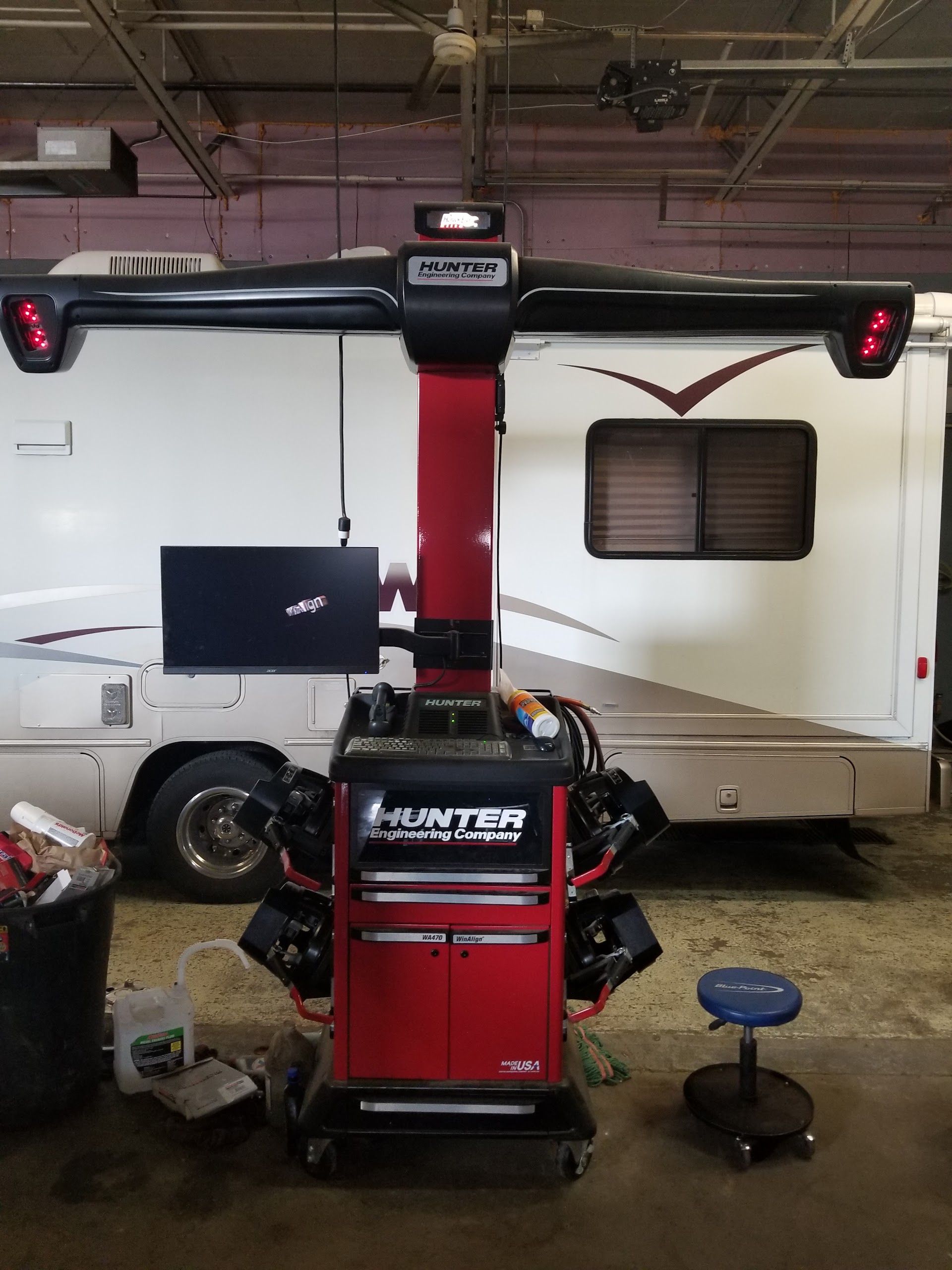 Red automotive lift in a garage bay with a small trailer and shop stool nearby | Lanning Automotive & Tire