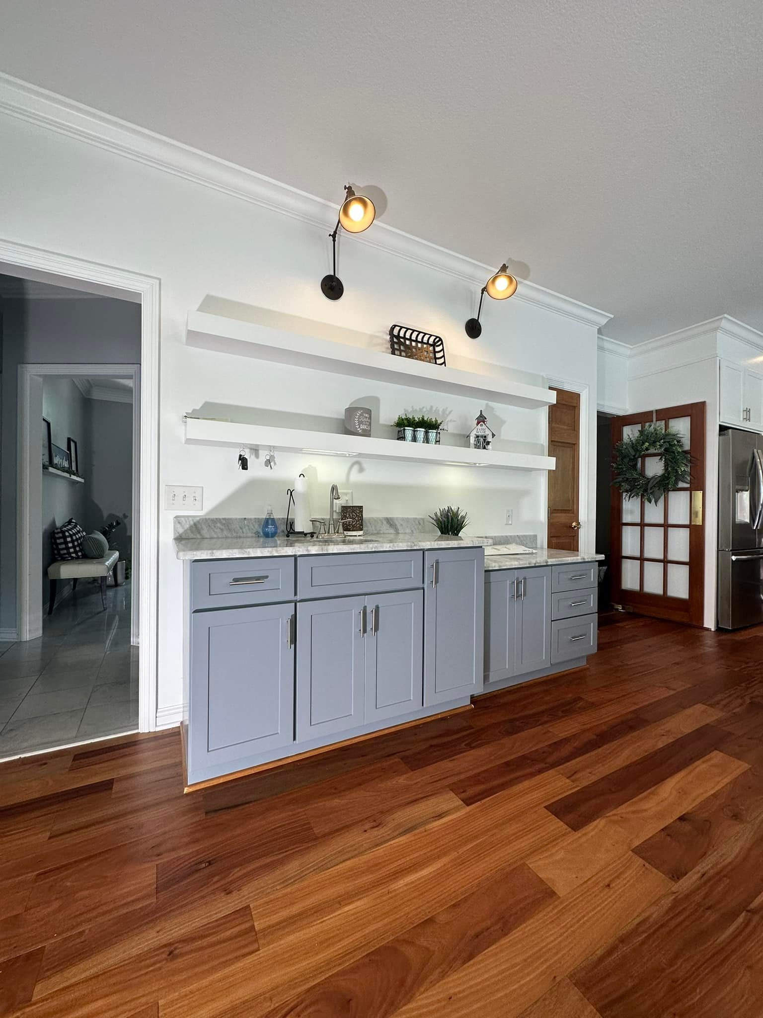 A home wet bar with gray cabinets, open shelving, and track lighting, set against a white wall with crown molding.