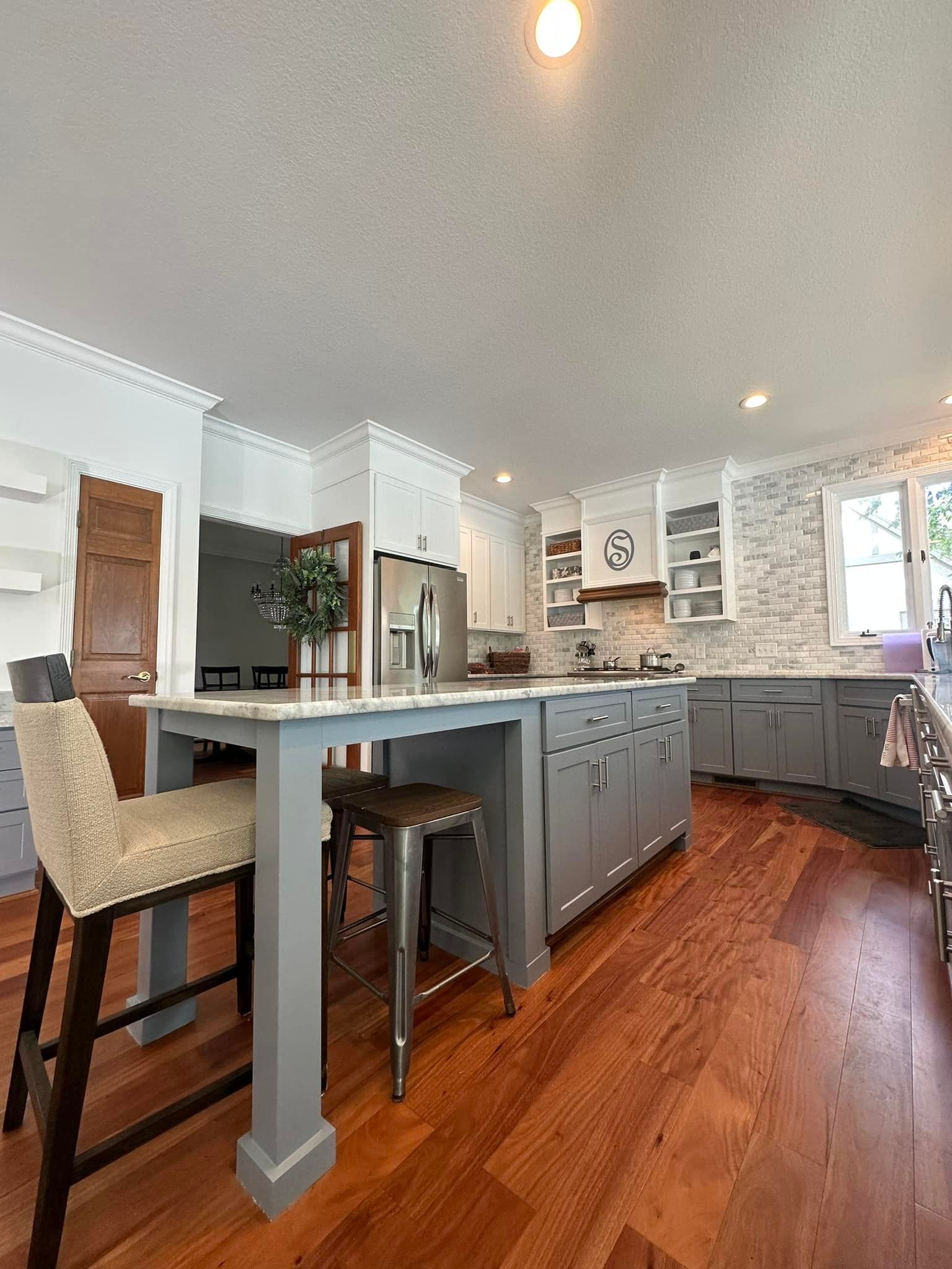 Kitchen with gray cabinets, white countertops, wood floors, and bar stools.