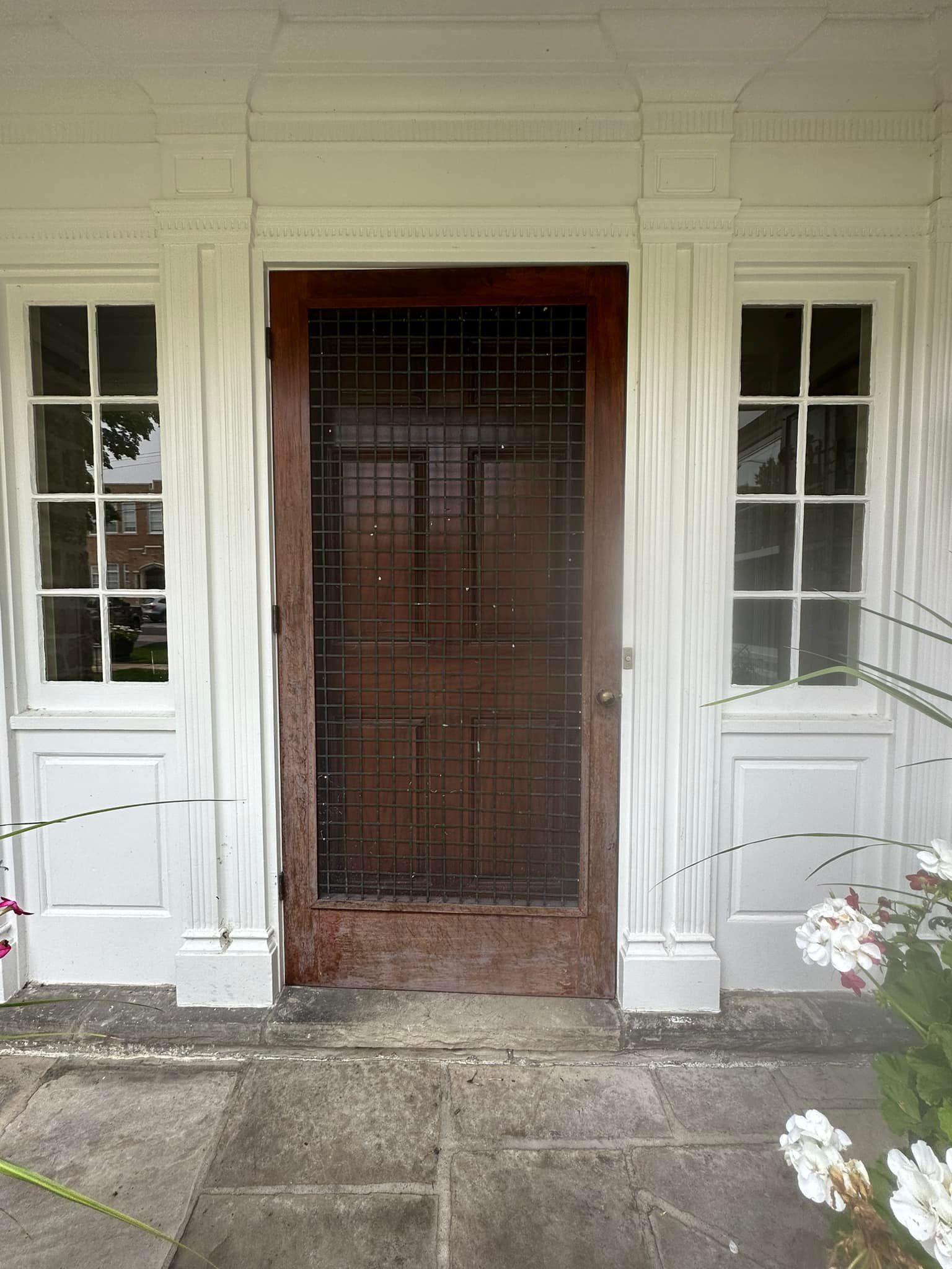 White front door with screen door, flanked by windows. Exterior of a white building.