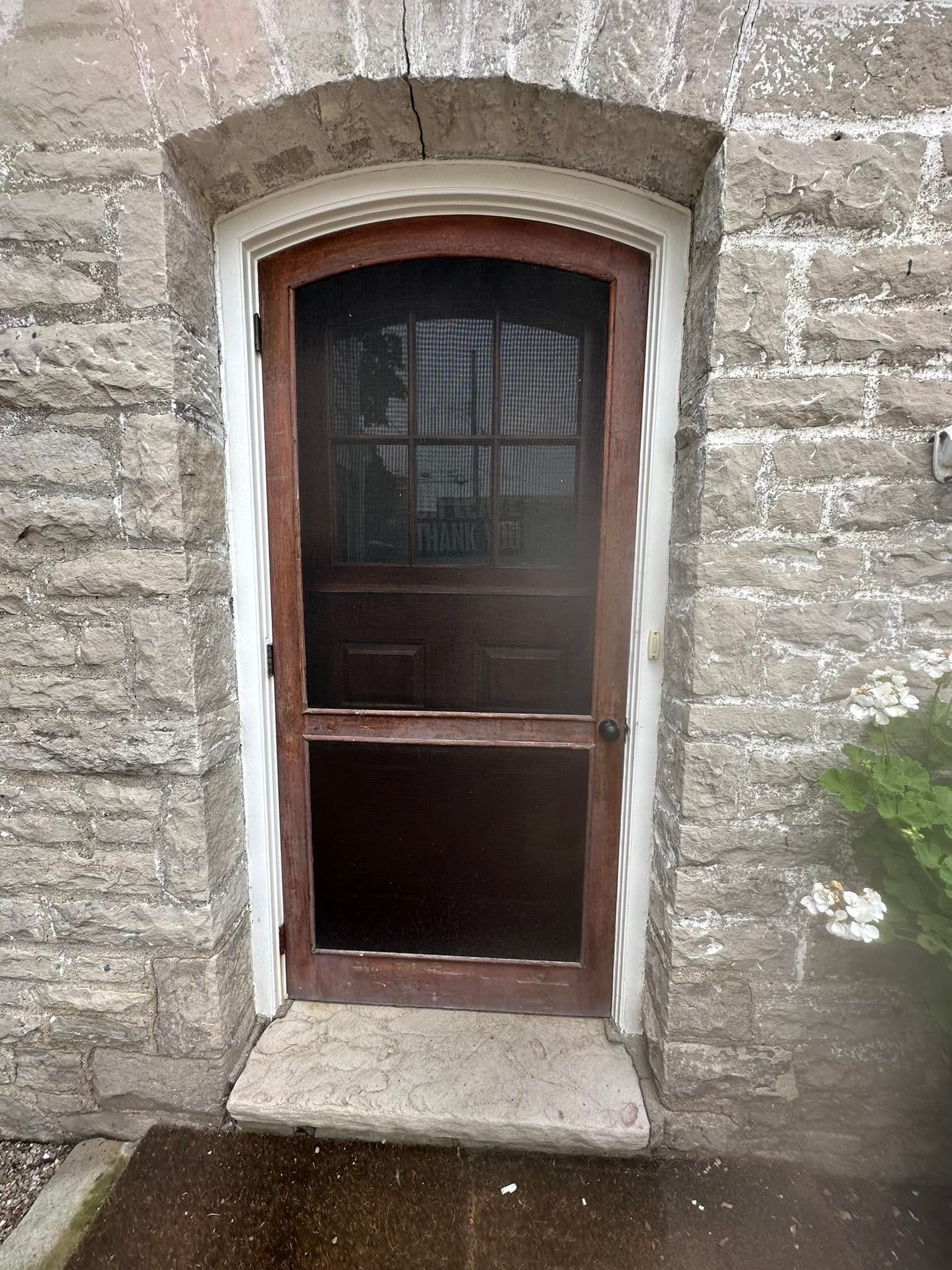 Brown wooden door with screen, set in stone wall, white trim.