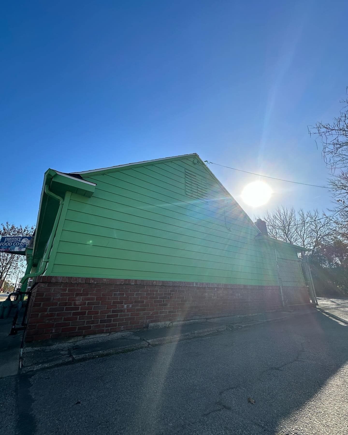 Green building with red brick base under a sunny blue sky.