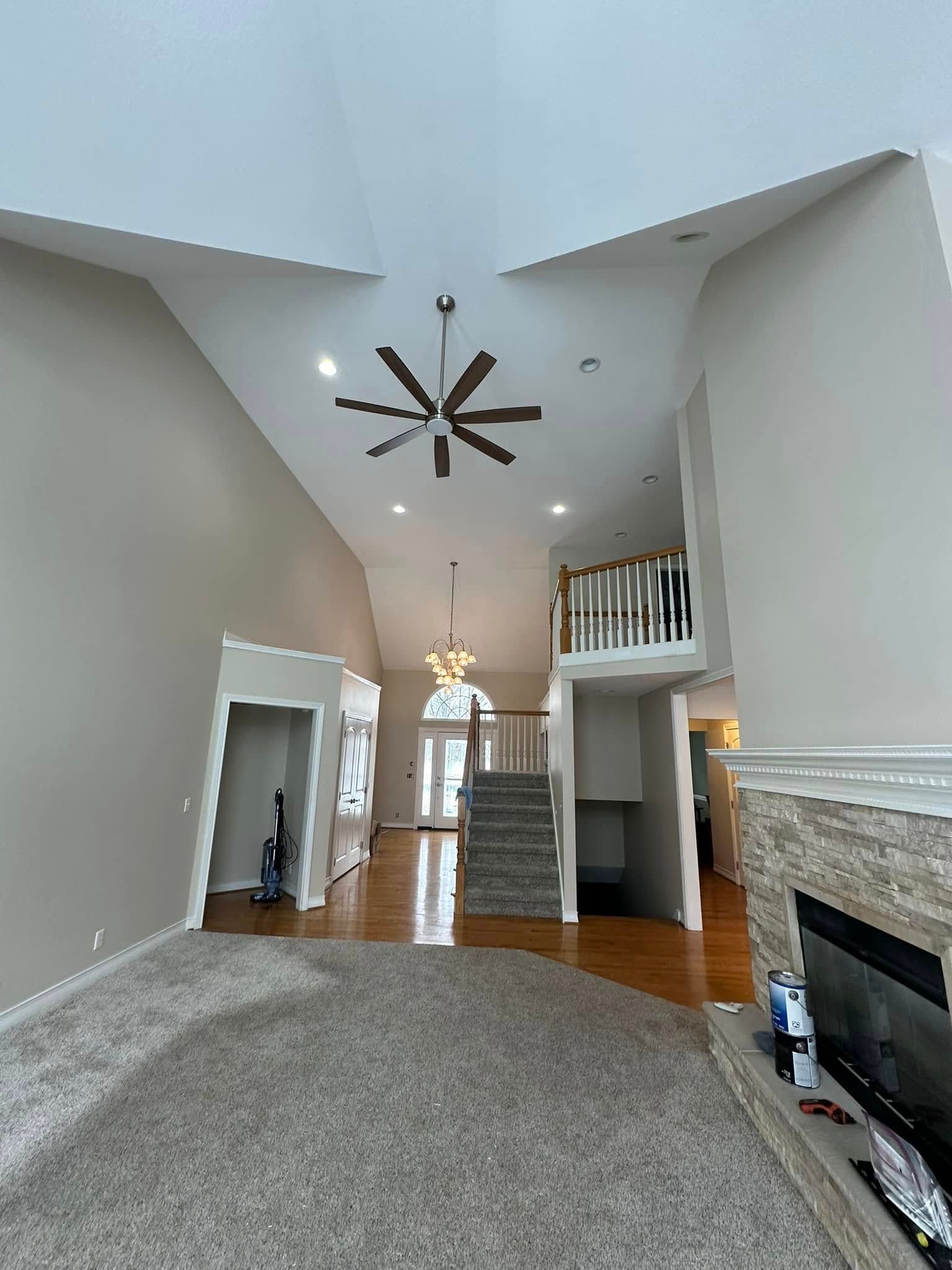 Spacious living room with high ceilings, fan, fireplace, and staircase to a balcony. Beig