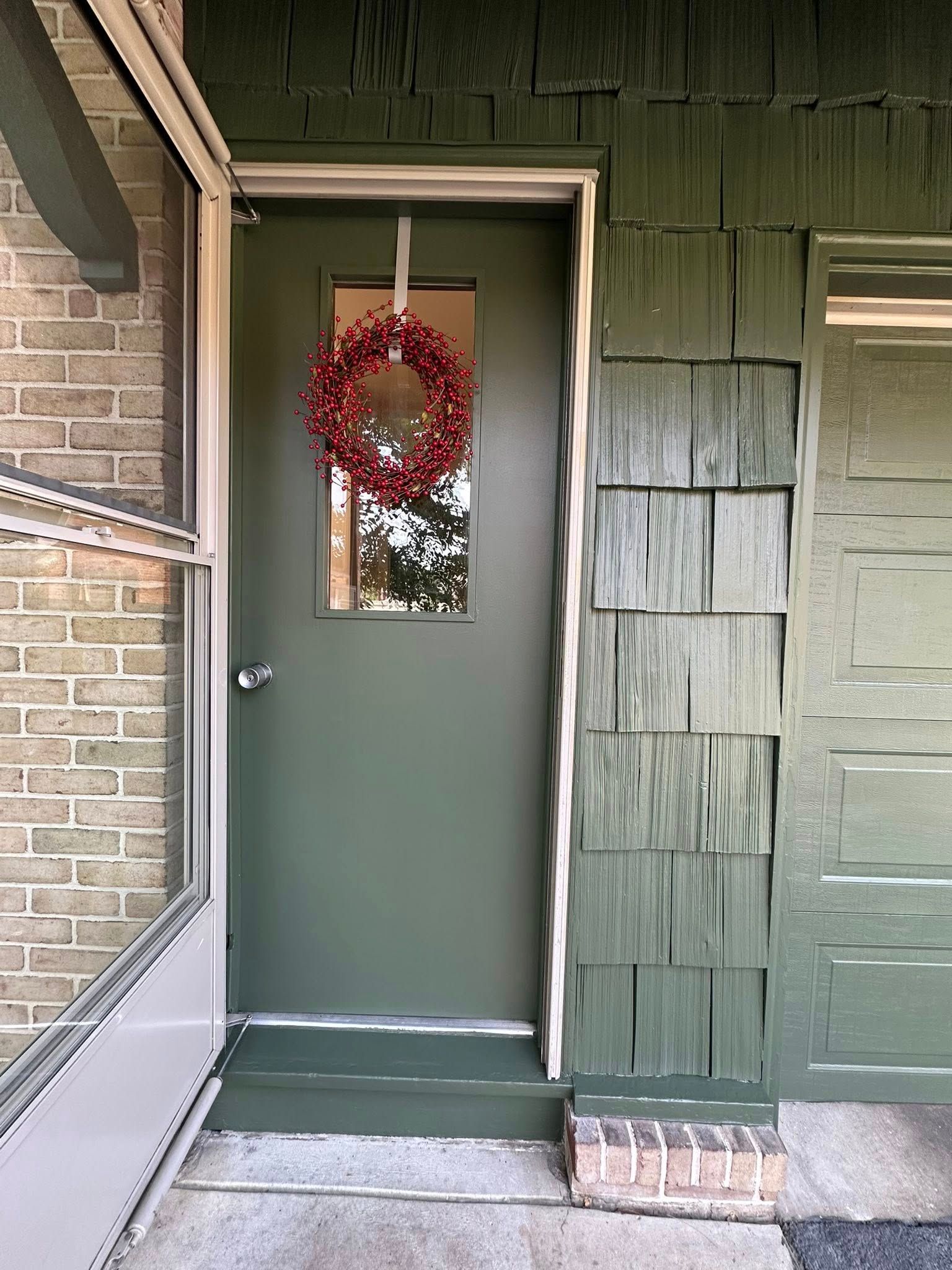 Green door with wreath, next to green shingled siding.