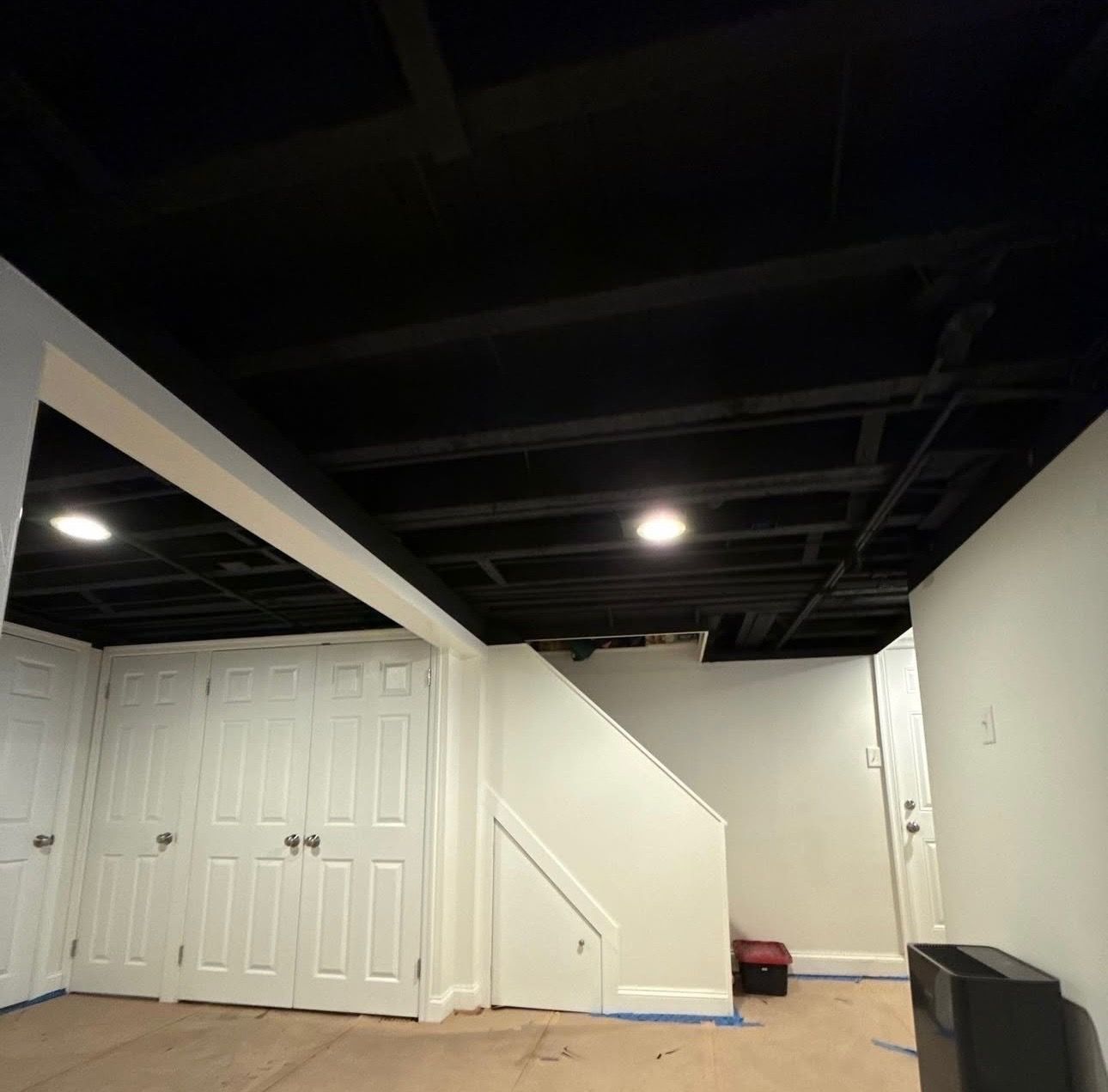 Interior view of a basement with wooden stairs, light flooring, laundry machines, and white walls.