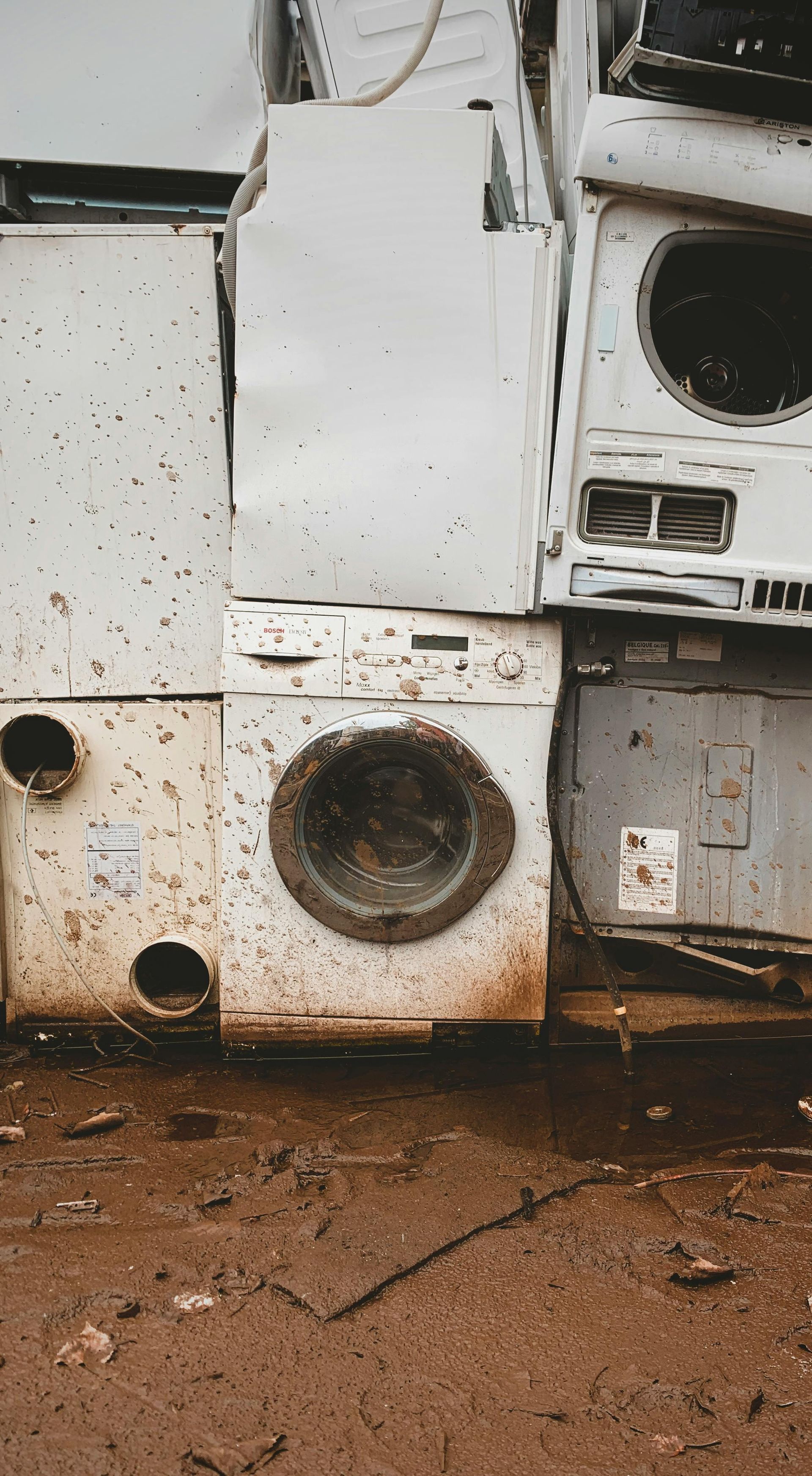 A bunch of old washing machines are stacked on top of each other on the ground.