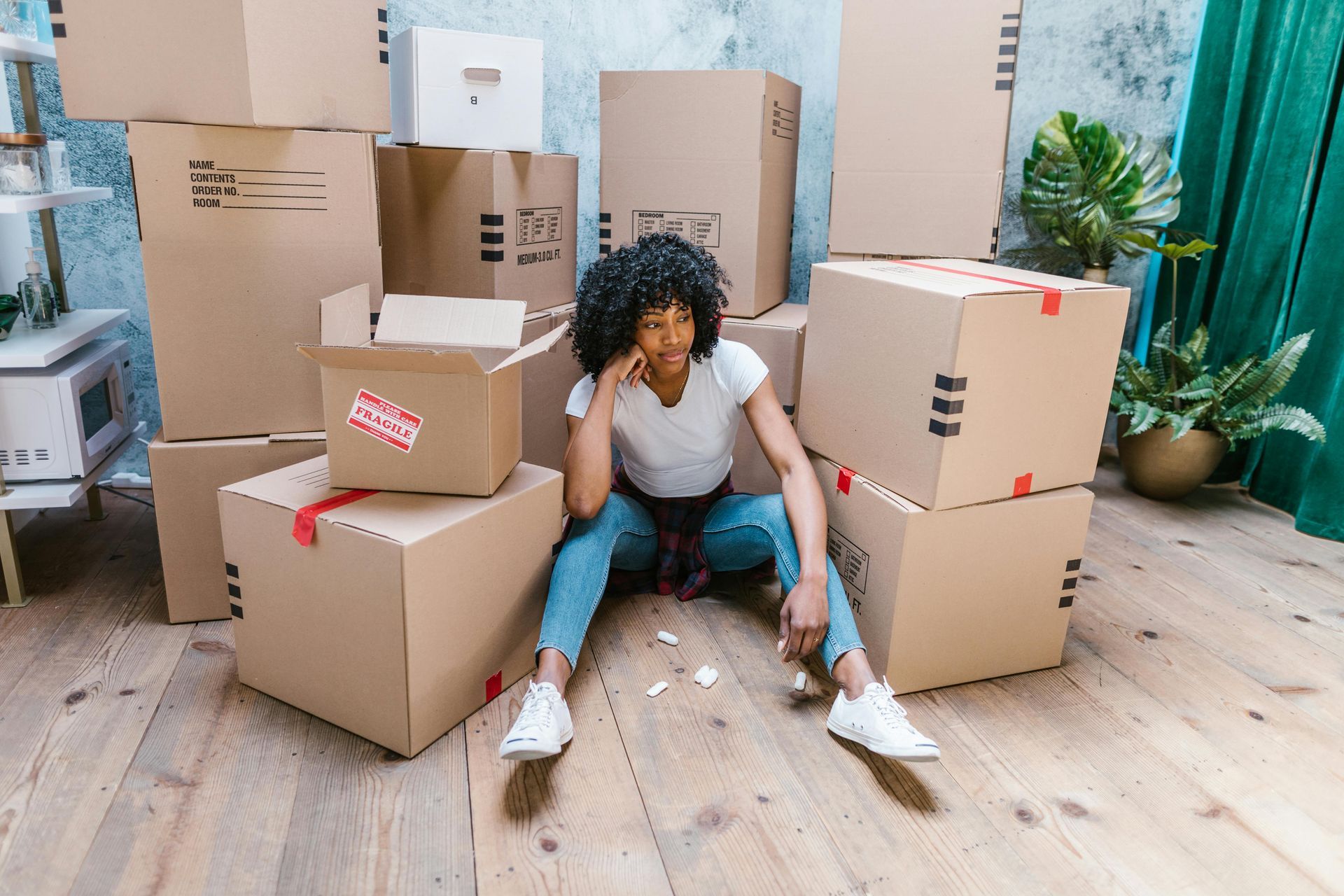 A woman is sitting on the floor surrounded by cardboard boxes.