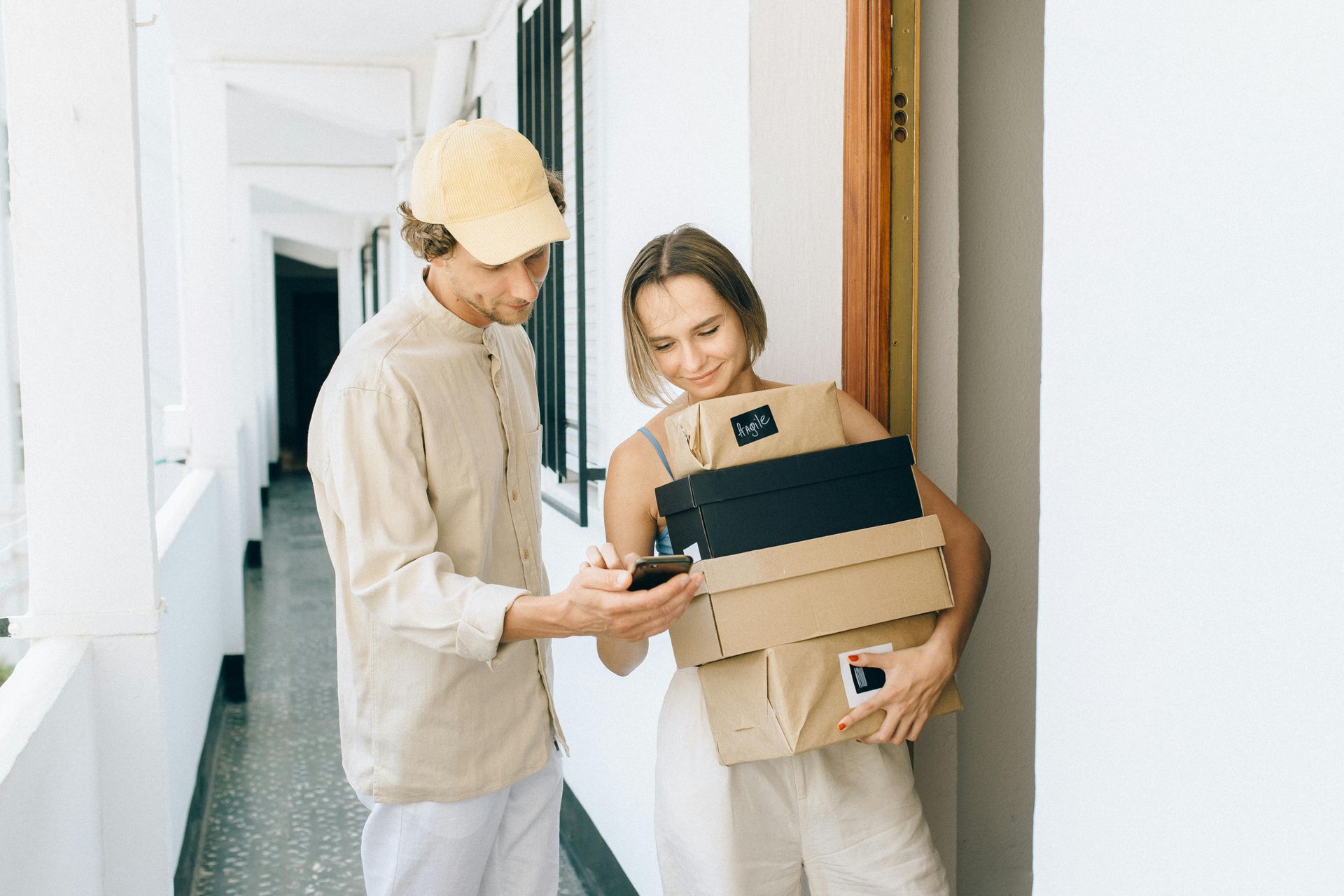 A delivery man is talking to a woman holding a stack of boxes.
