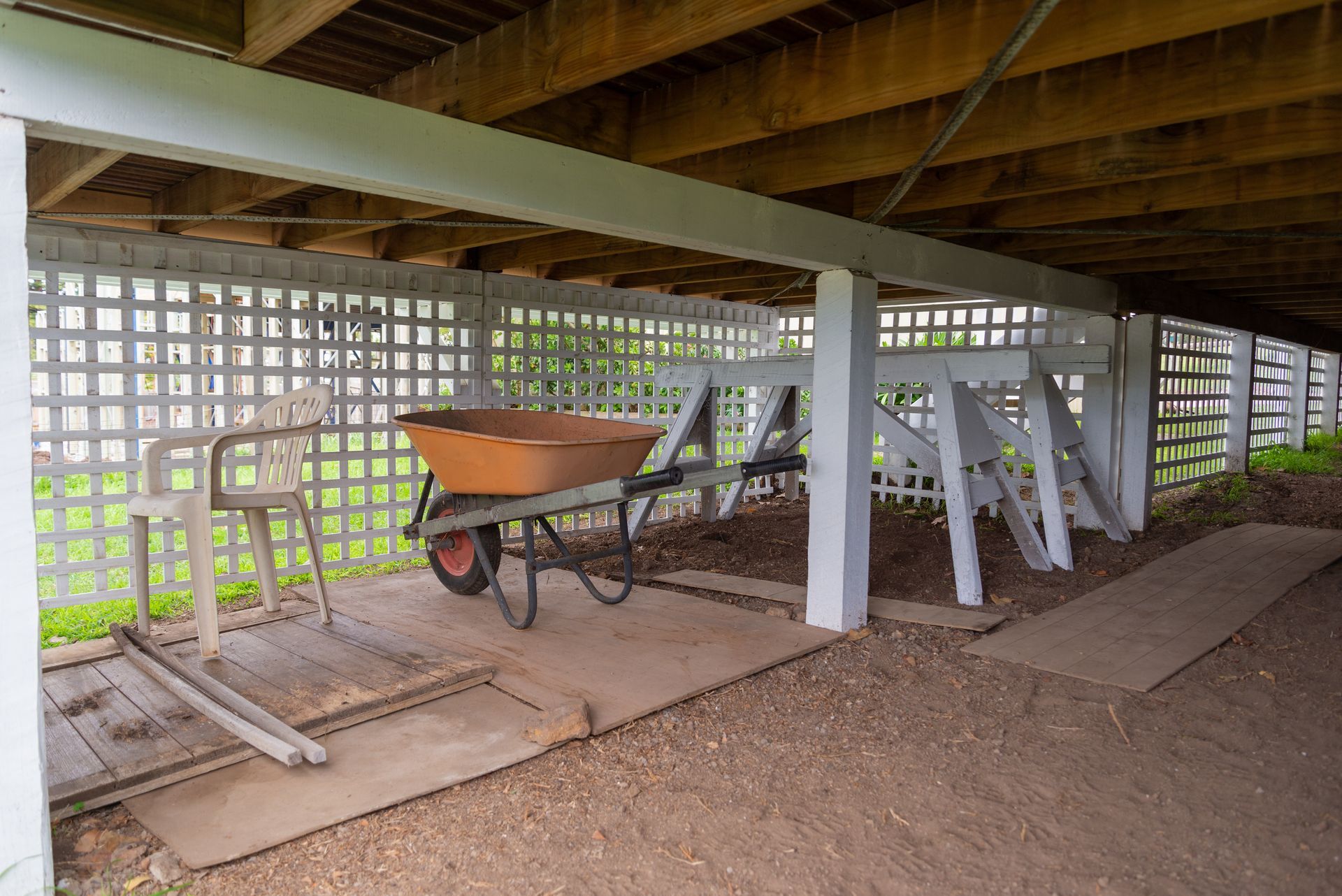 A wheelbarrow positioned beneath a covered porch propped up by wooden stumps.