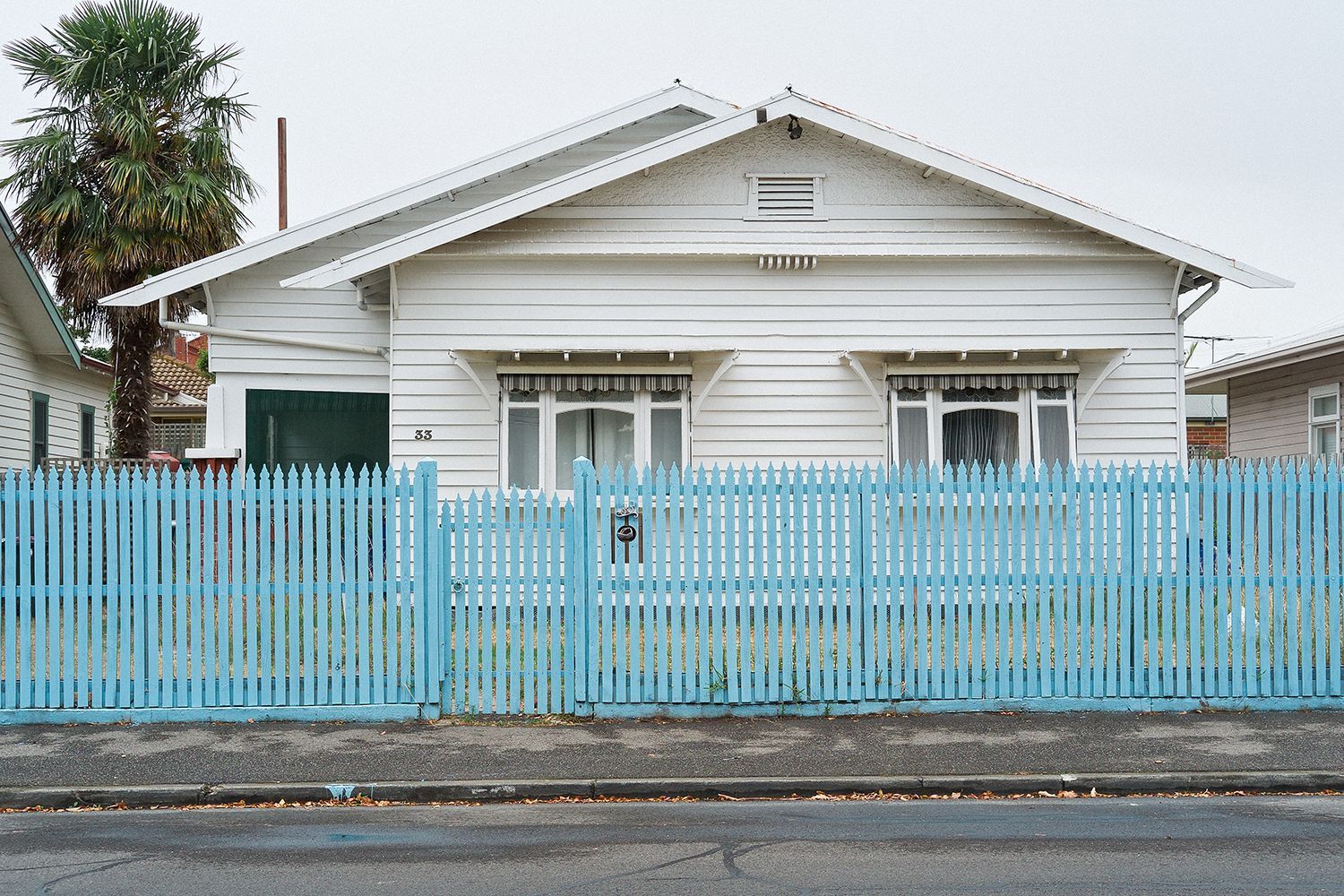 A suburban weatherboard house behind a blue picket fence. A suburban weatherboard house behind a blue picket fence.