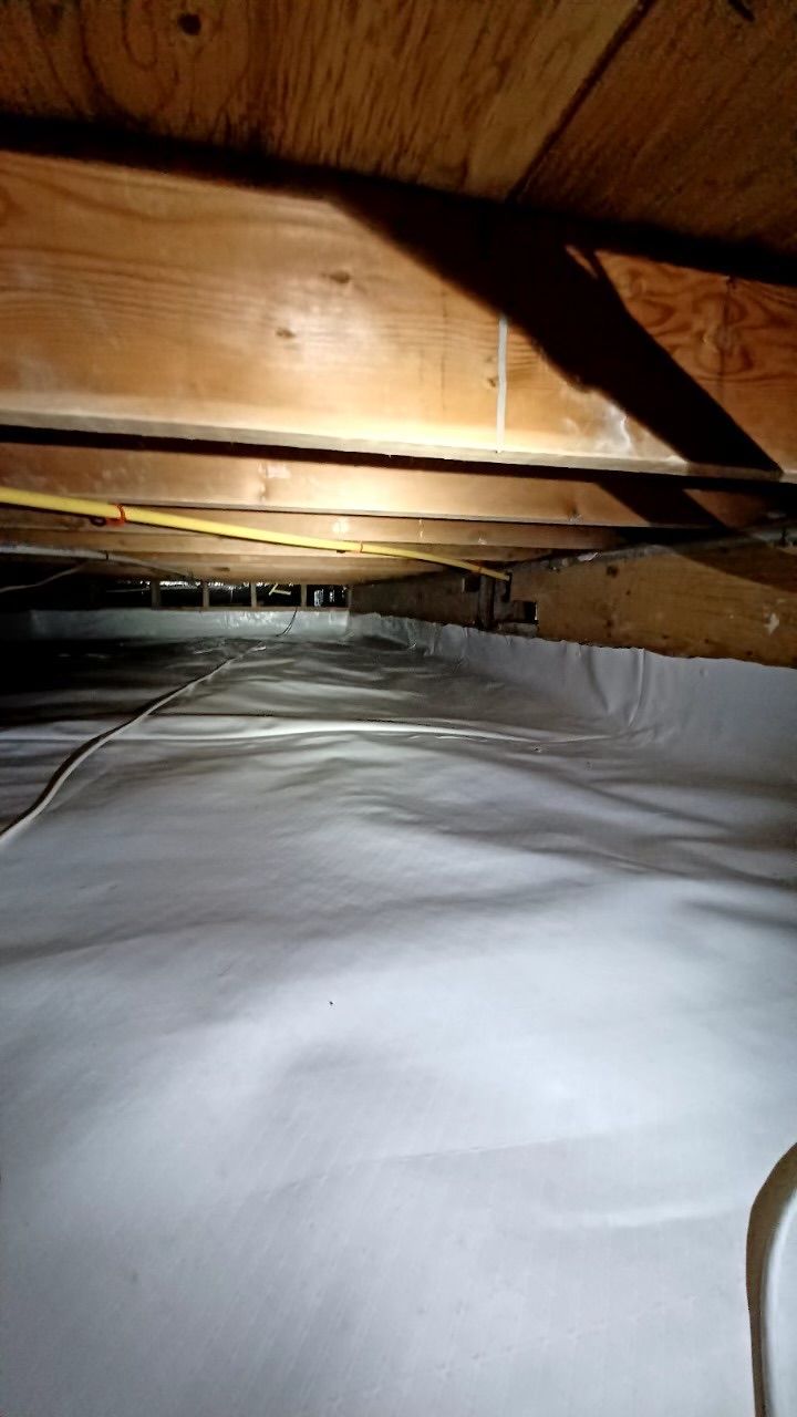 Dim attic crawlspace with insulation on the floor and wooden beams overhead.
