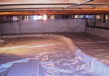 Plastic-covered crawl space under a house with wooden beams and exposed wiring