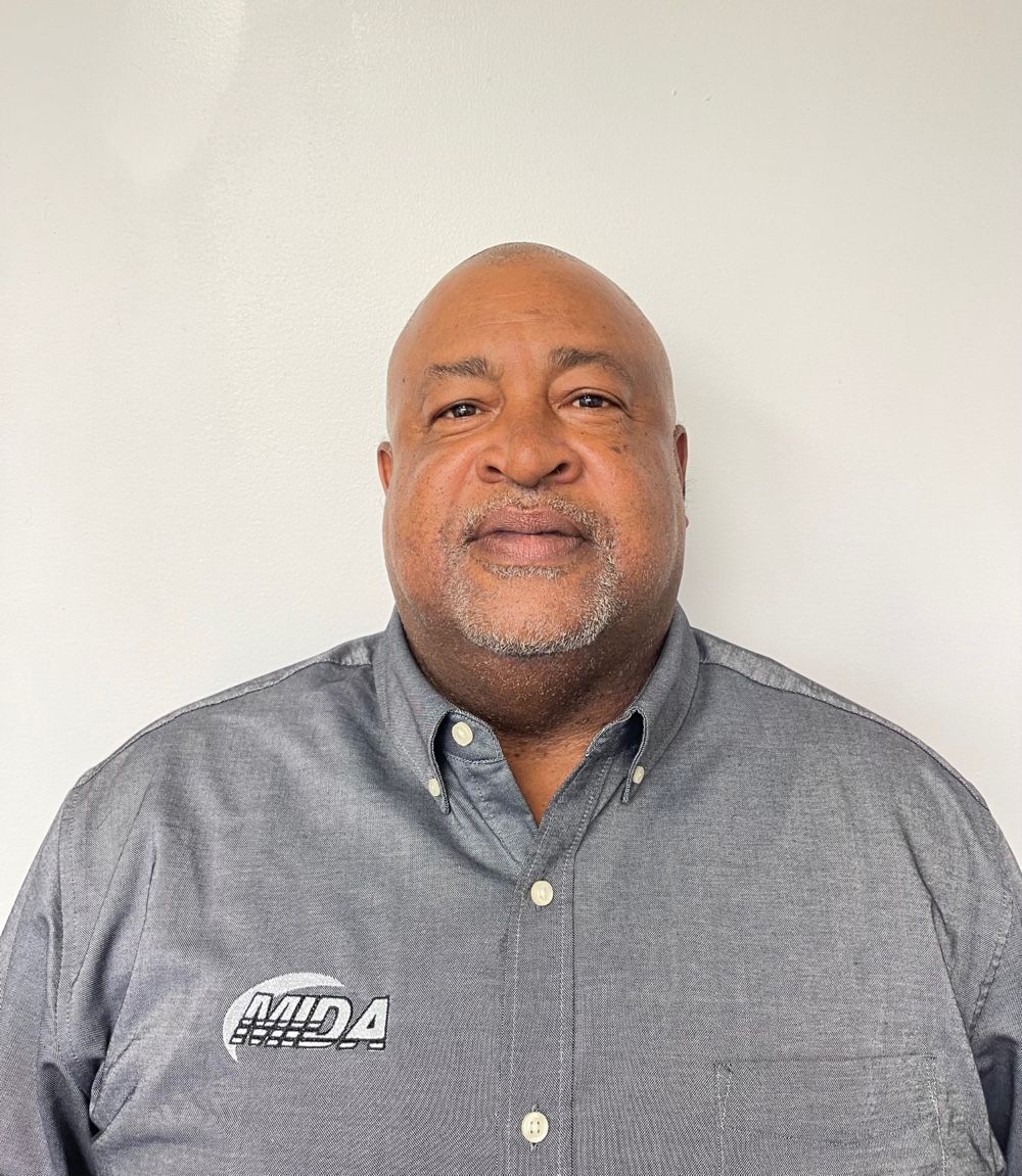 Smiling man in a gray button-down shirt against a plain light background