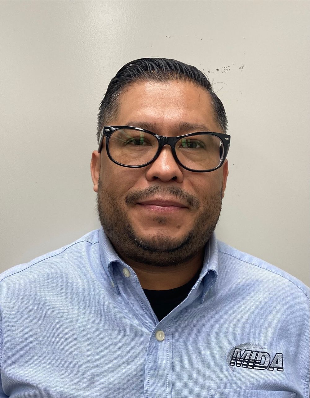 Portrait of a man wearing glasses and a light blue button-up shirt against a plain wall.