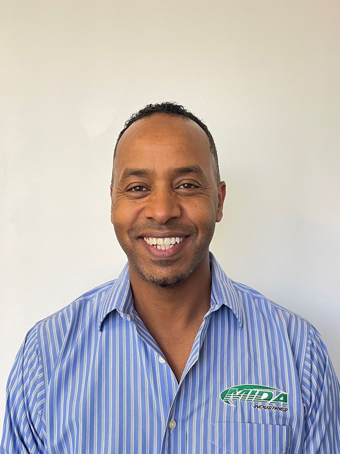 Smiling man in a blue striped shirt against a plain white wall
