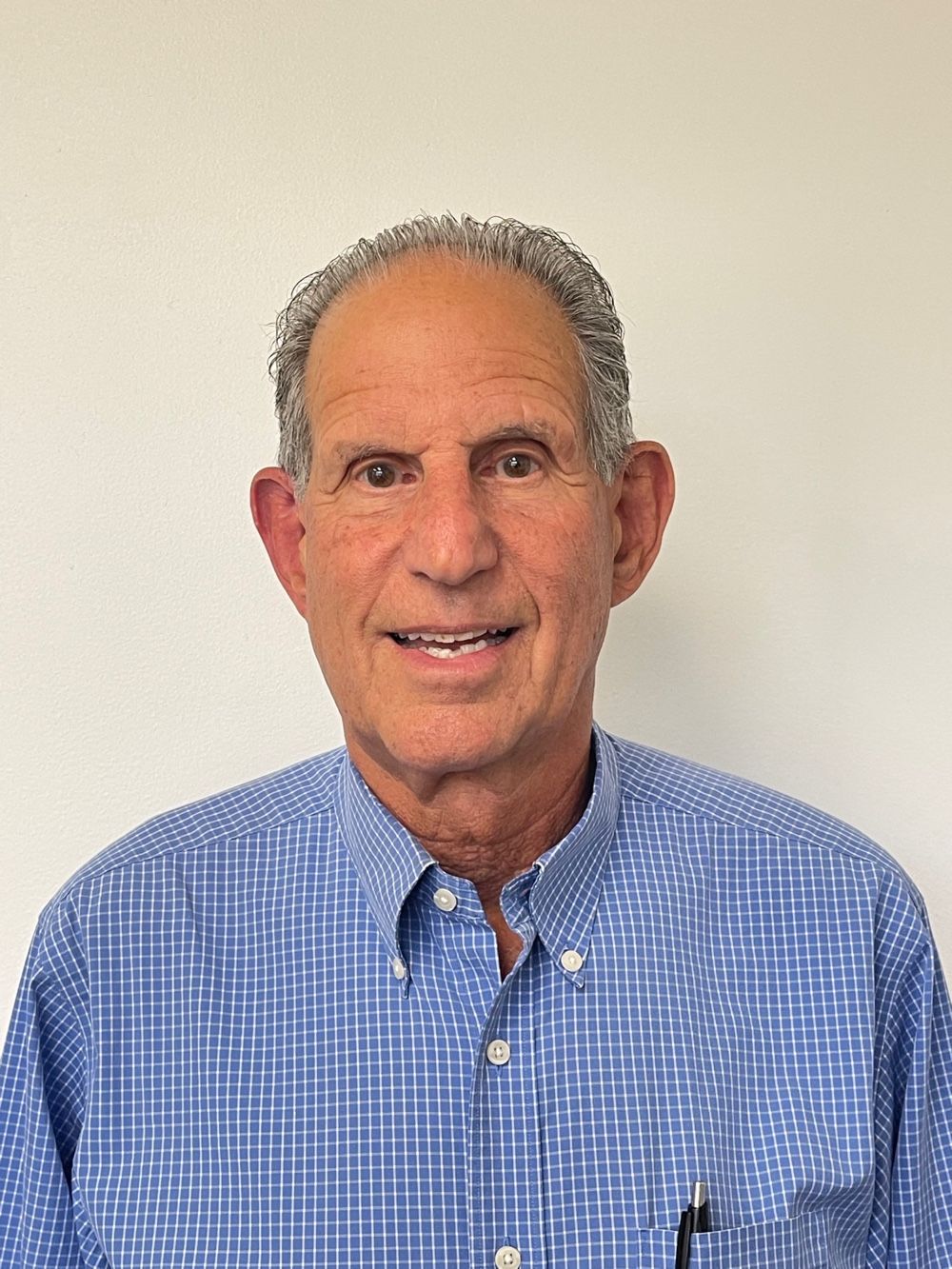 Smiling man in a blue checkered shirt against a plain light wall