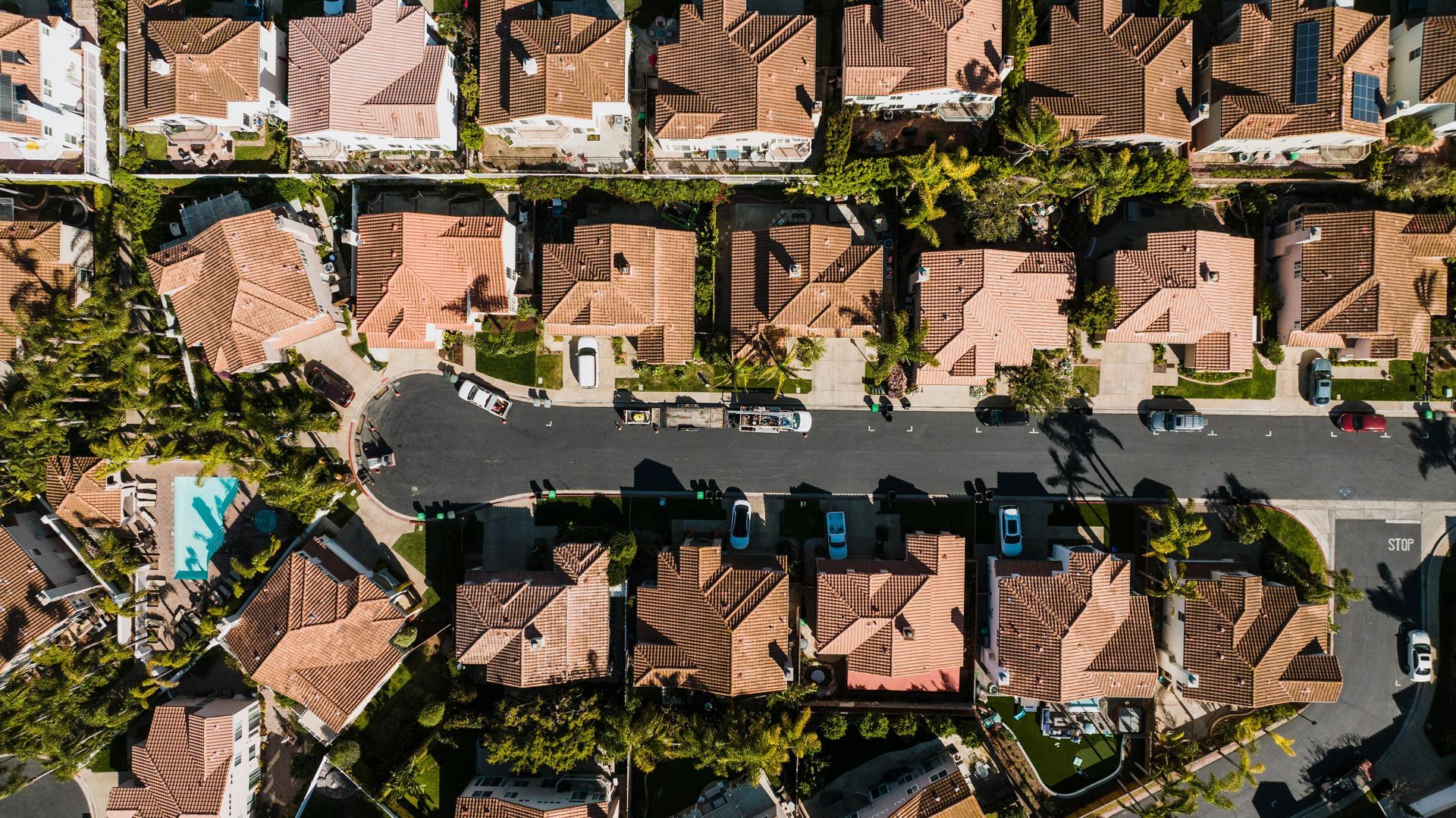 Aerial view of a residential street lined with palm trees and terracotta-roofed homes.