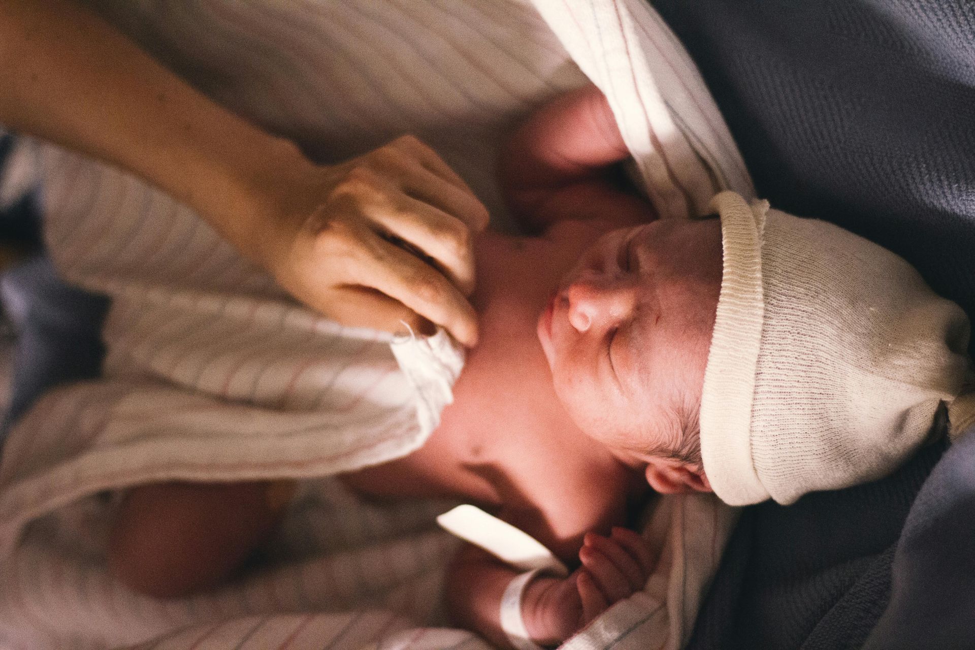 A newborn baby wearing a white hat is being examined by a person.