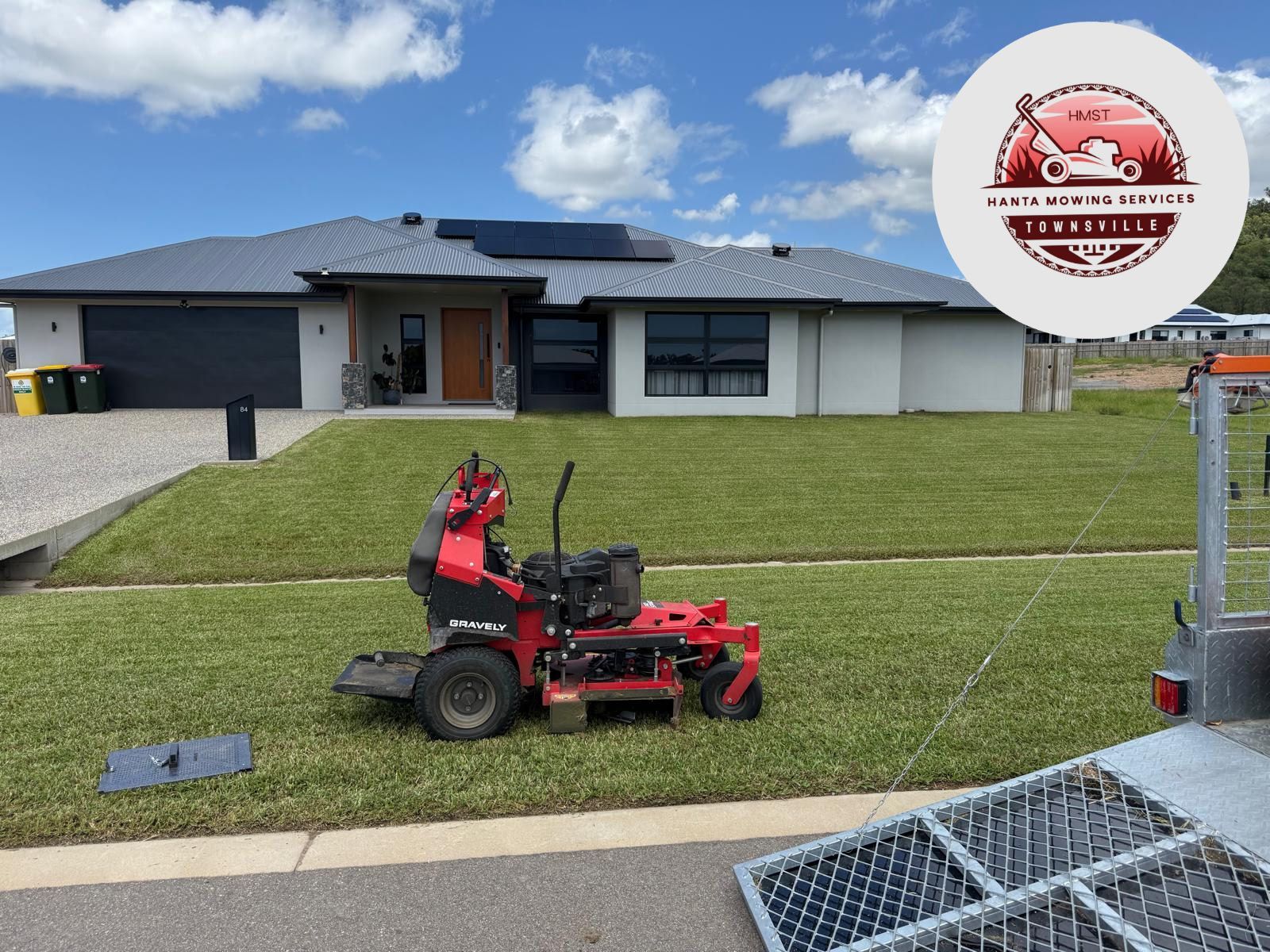 Red Lawnmower on Green Grass, in Front of a House With a Logo in the Corner — Hanta Mowing Services Townsville in Kirwan, QLD