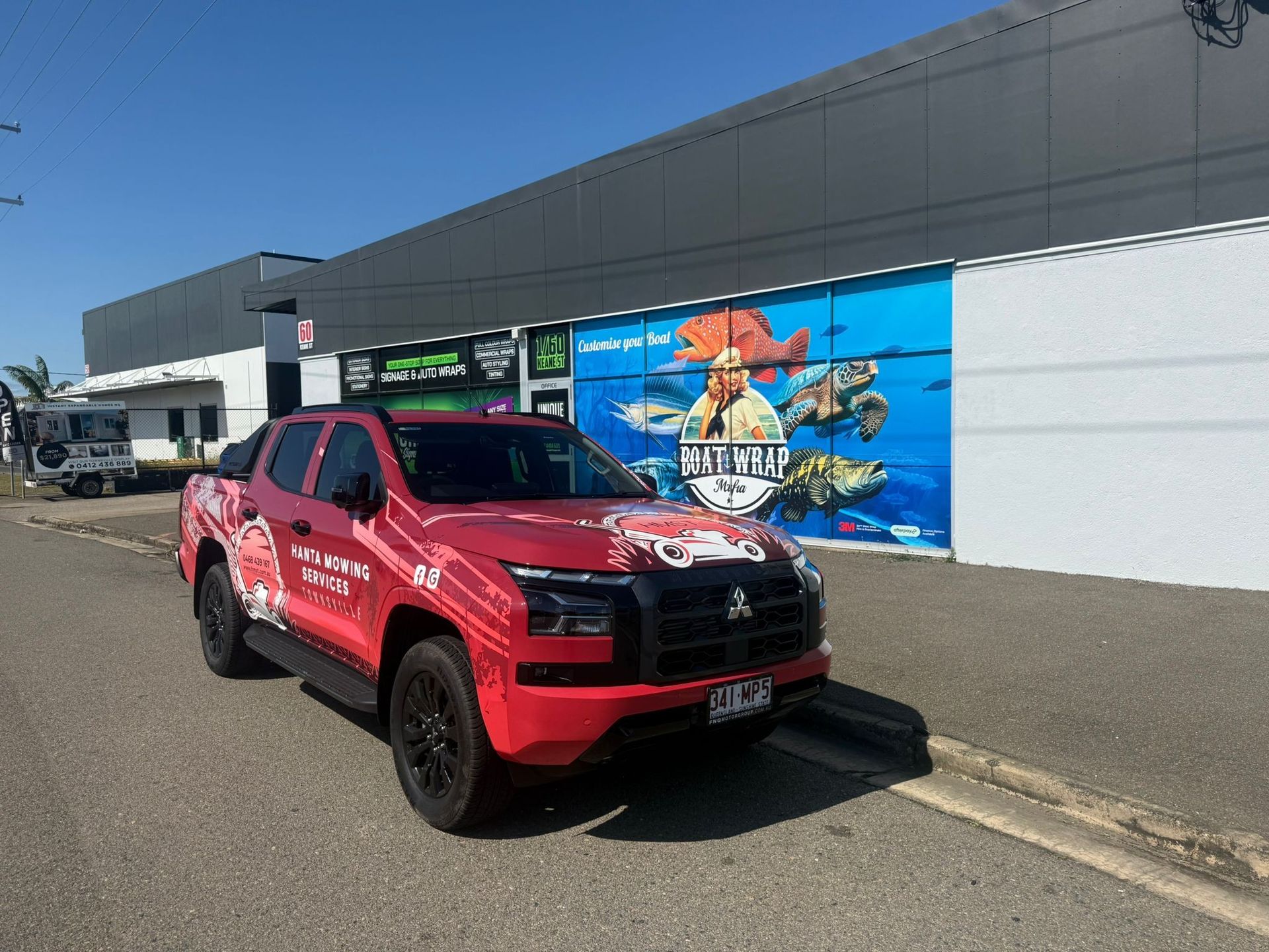 Red Truck With Logo Parked Outside a Building Featuring an Underwater Mural — Hanta Mowing Services Townsville in Kirwan, QLD