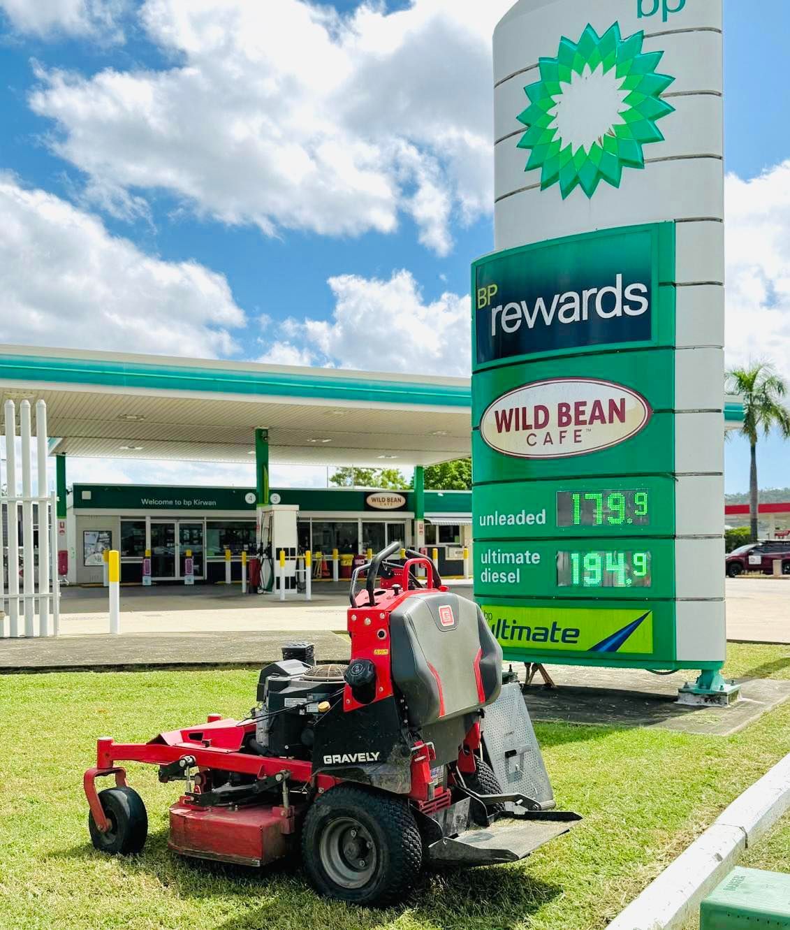 Red Lawnmower in Front of a Bp Gas Station With Fuel Prices Displayed — Hanta Mowing Services Townsville in Kirwan, QLD
