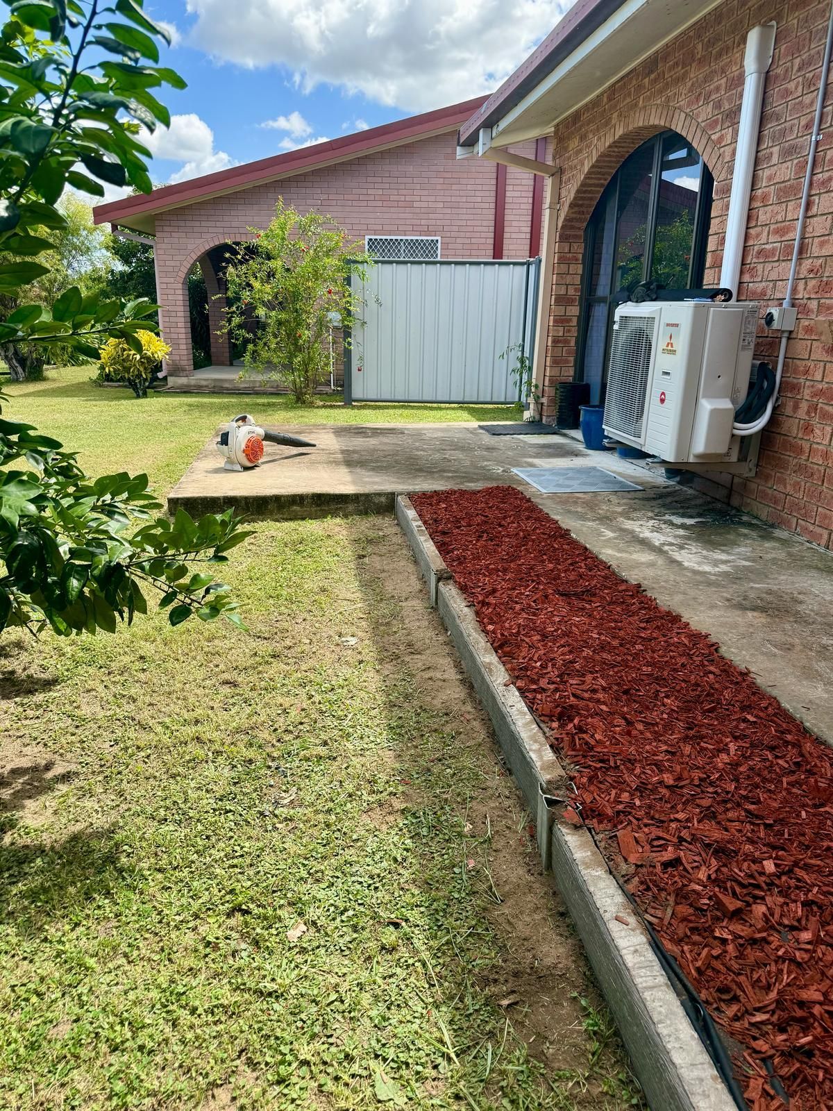 Red Mulch Pathway Next to Green Lawn, With Brick Building — Hanta Mowing Services Townsville in Kirwan, QLD