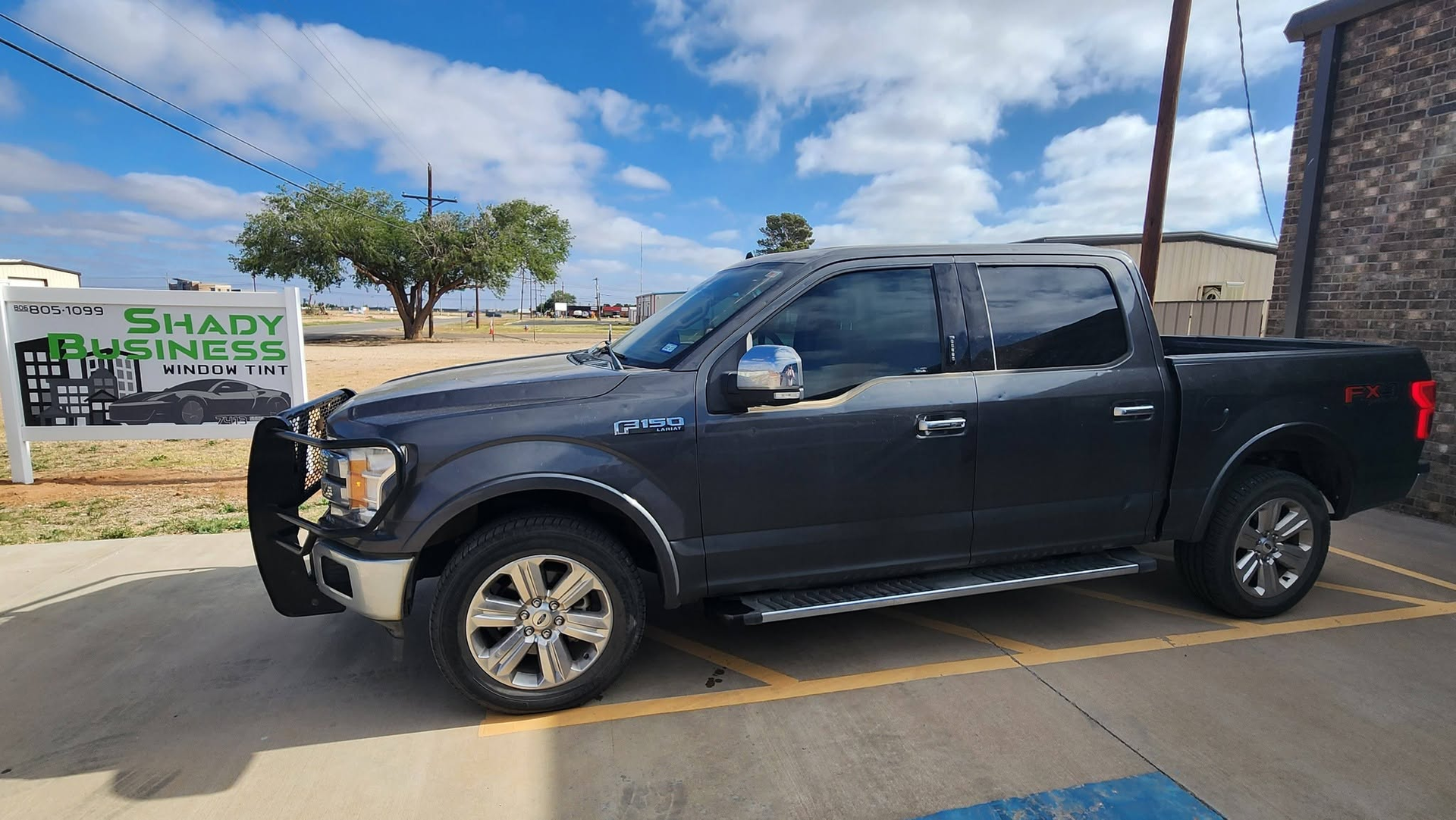 Black pickup truck parked outdoors near a roadside sign and stone wall under a blue sky