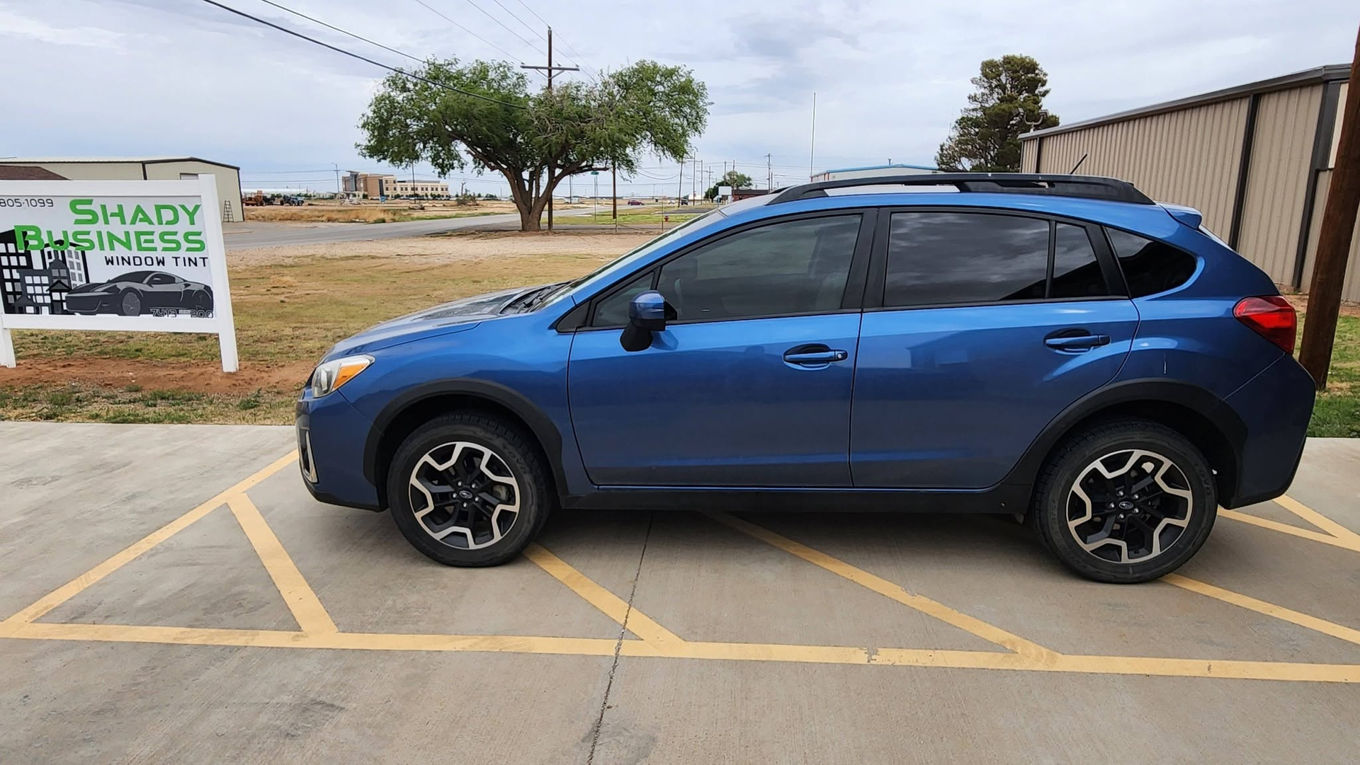 Blue compact SUV parked in a lot beside a roadside sign on a cloudy day