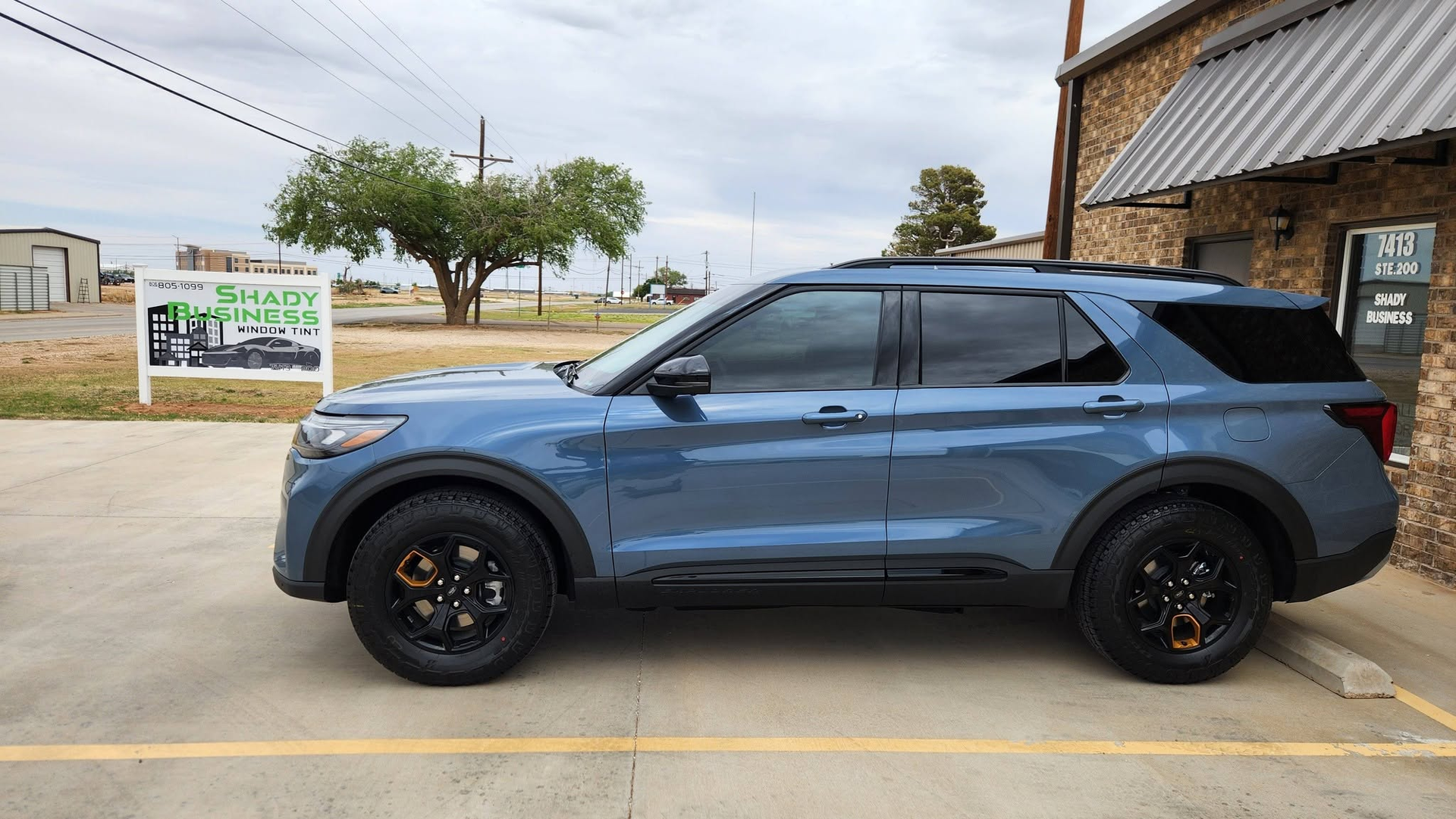 Blue SUV parked in a lot beside a tree and roadside sign under cloudy skies