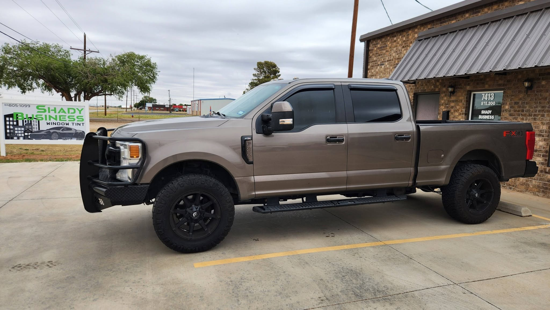 Tan pickup truck parked outside a brick building on a cloudy day.