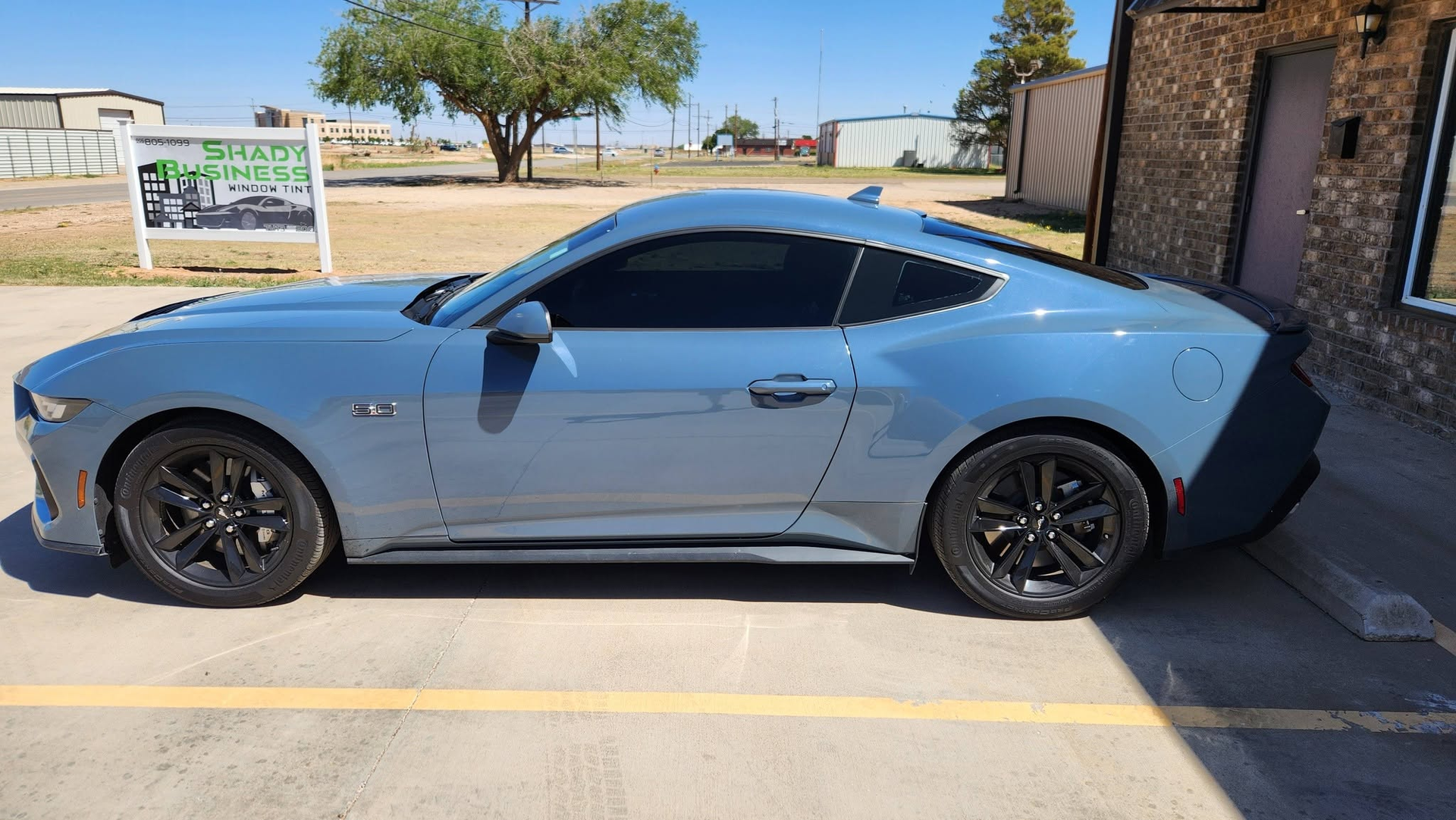 Blue sports coupe parked beside a building in a sunny outdoor lot