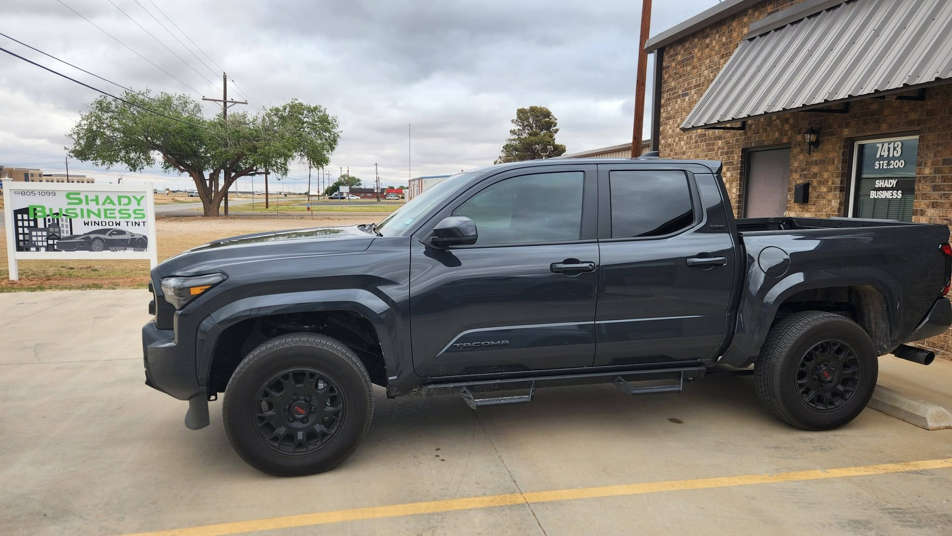 Black pickup truck parked beside a brick building on a cloudy day