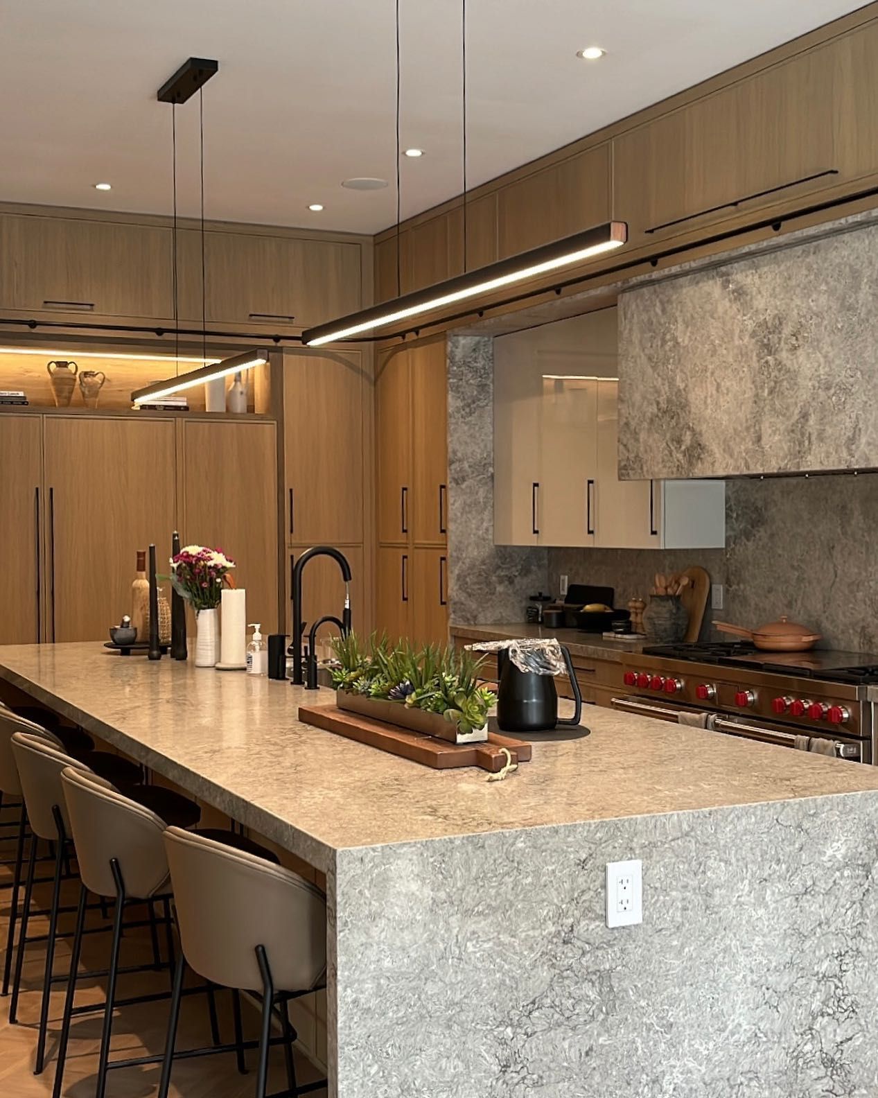 Modern kitchen with wood cabinets, stone island, pendant light, and bar stools