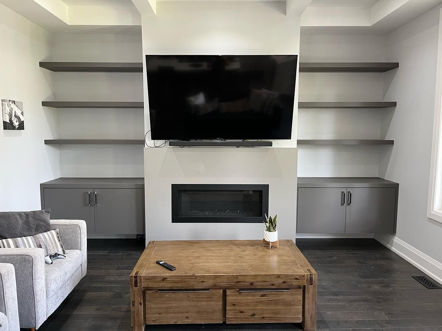 Modern living room with TV over fireplace, built-in shelves, gray cabinets, and a wooden coffee table.