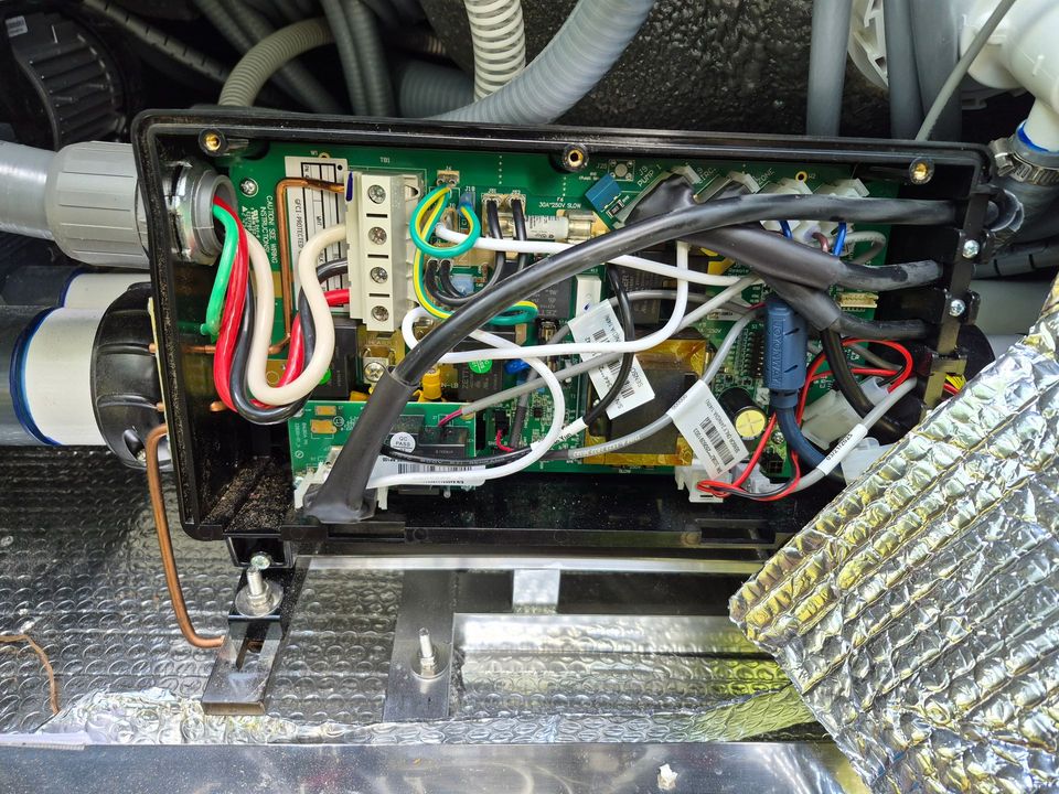 Electrician in hard hat and hi-vis vest inspecting an open electrical panel with a tablet