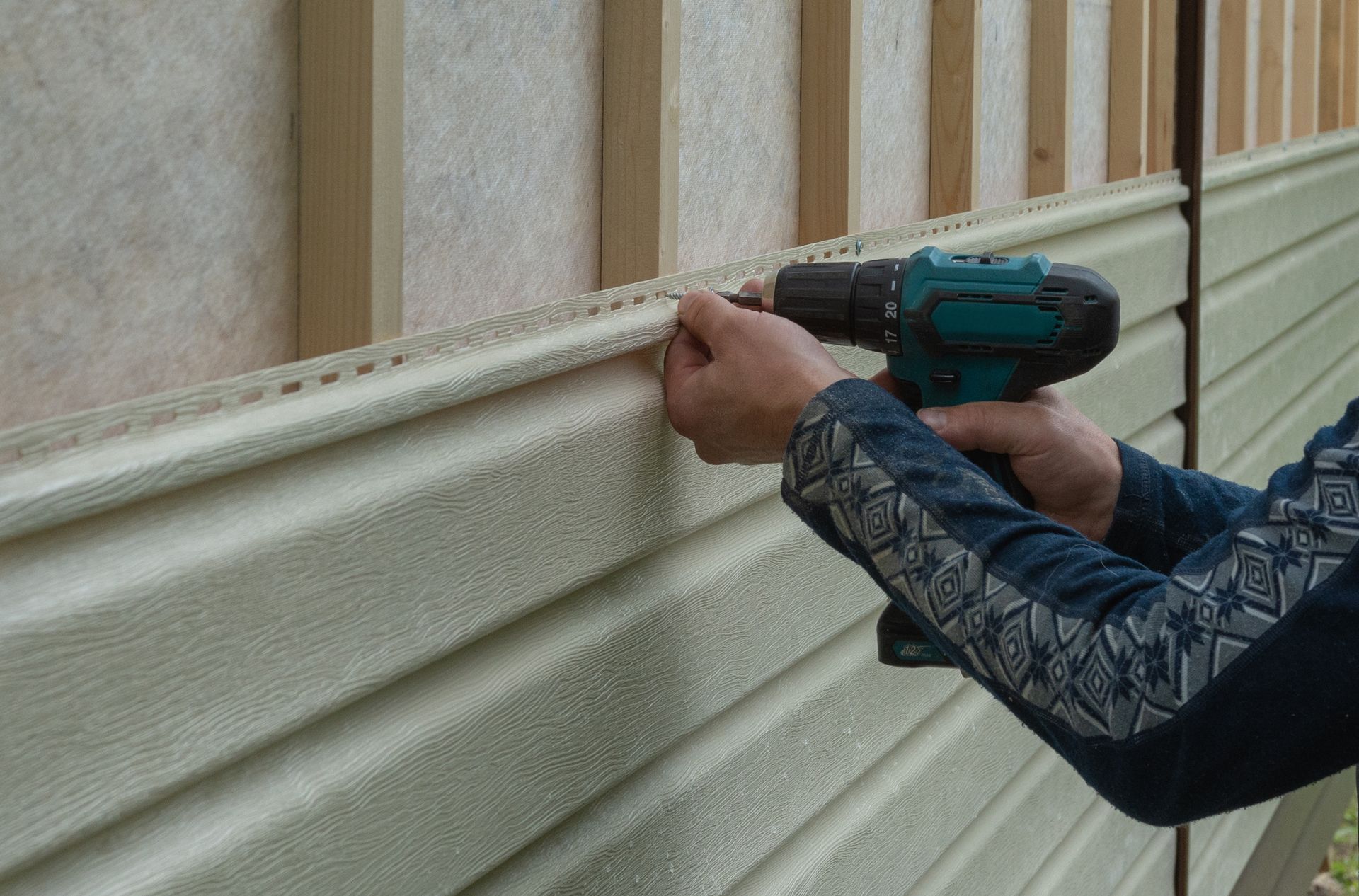 Worker using a cordless drill to install vinyl siding panels on a house exterior