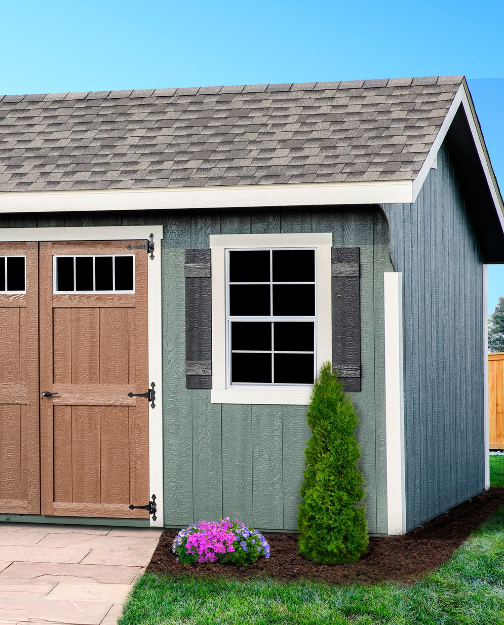 A small shed with a wooden door and windows is sitting in the middle of a lush green yard.