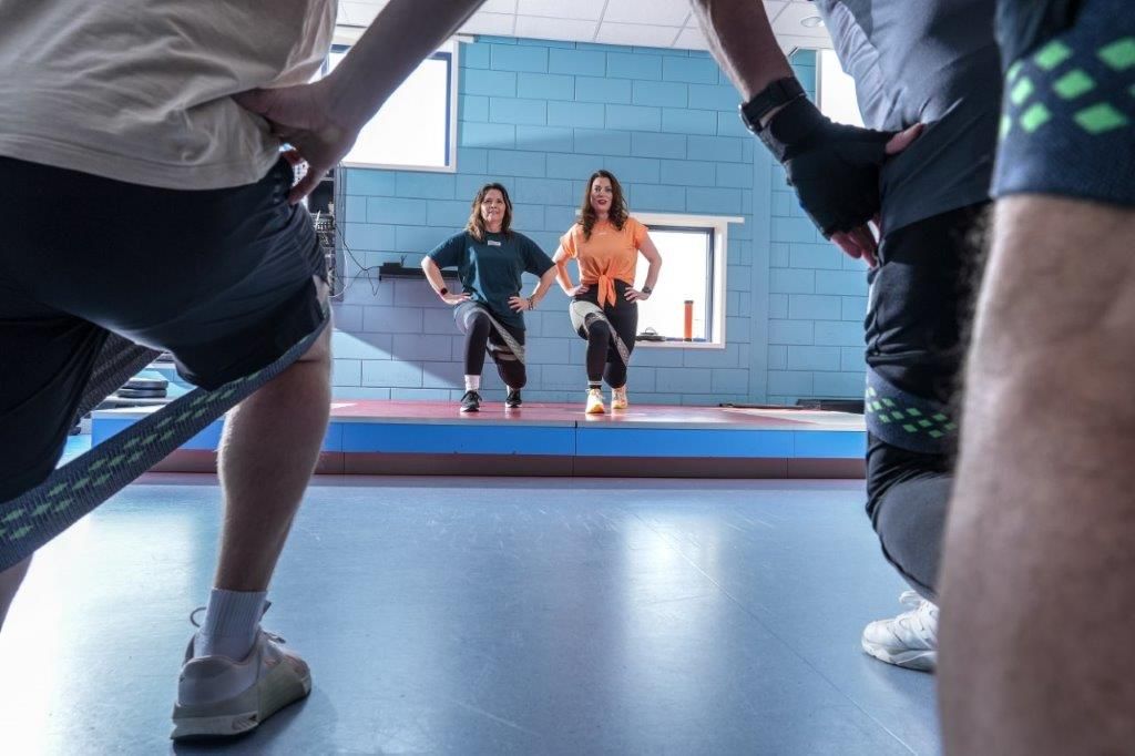 Mensen oefenen met weerstandsbanden, twee vrouwen op de achtergrond, indoor sportschool.