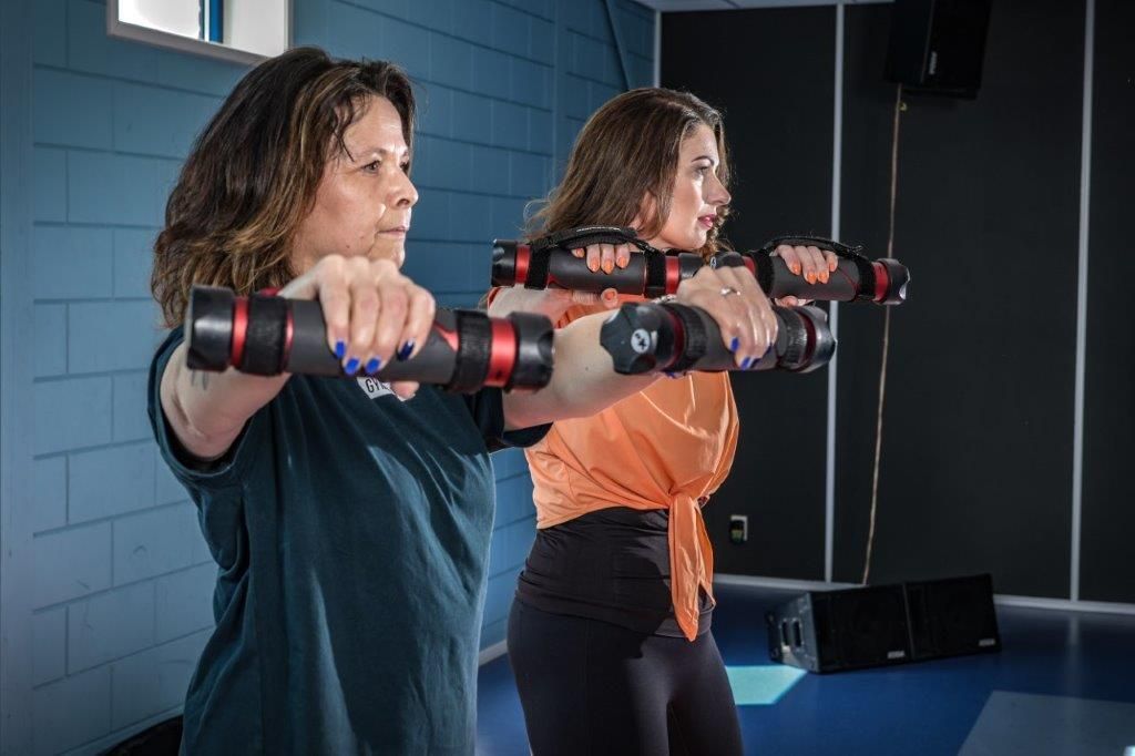 Twee vrouwen trainen met zwarte en rode halters in een blauwe sportschool.