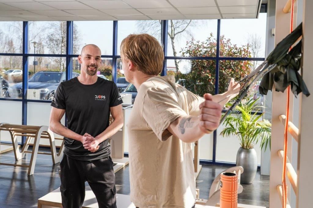 Man helpt iemand met oefeningen met behulp van een weerstandsband in een lichte kamer.