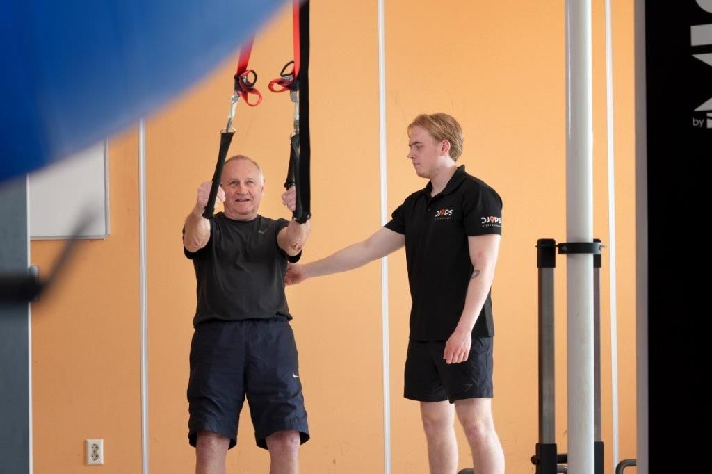 Man doet suspension training met hulp van een trainer in een sportschool.