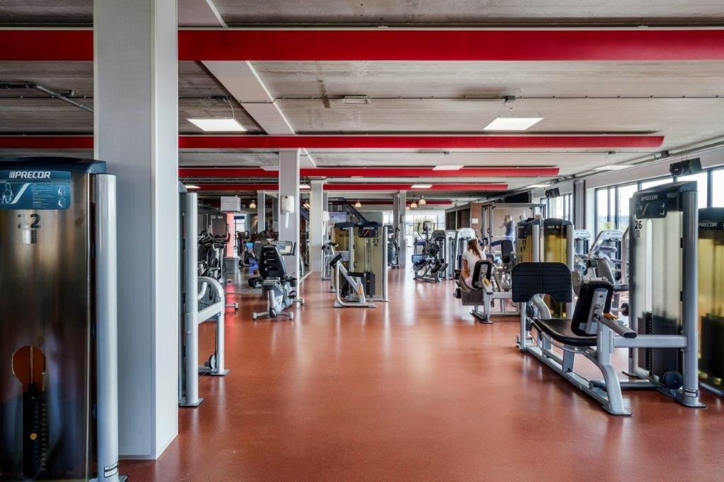 Interieur van een sportschool met gewichten op een rode vloer en rode plafondaccenten.